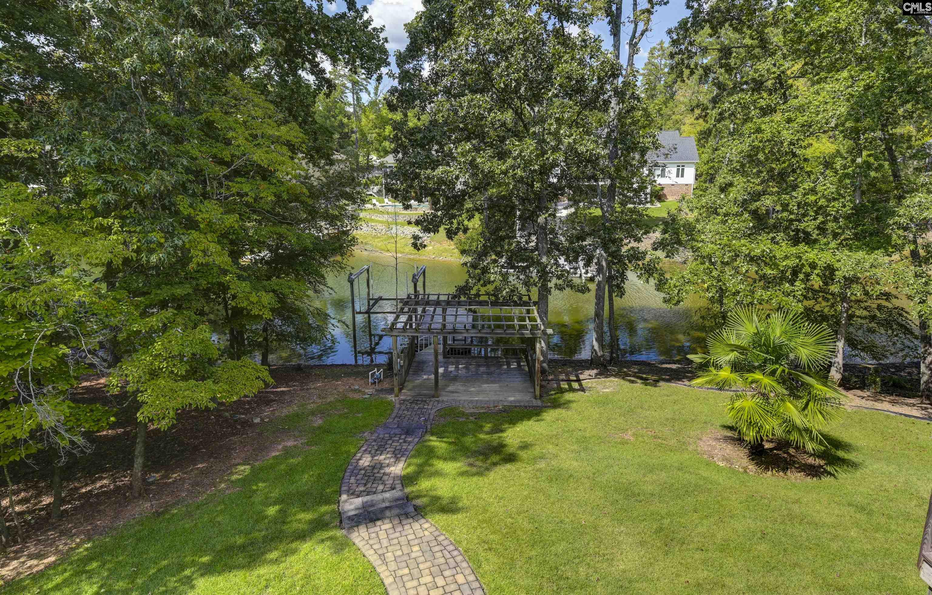 Waterfront backyard with a curved paver path leading to a wooden dock beneath mature trees.