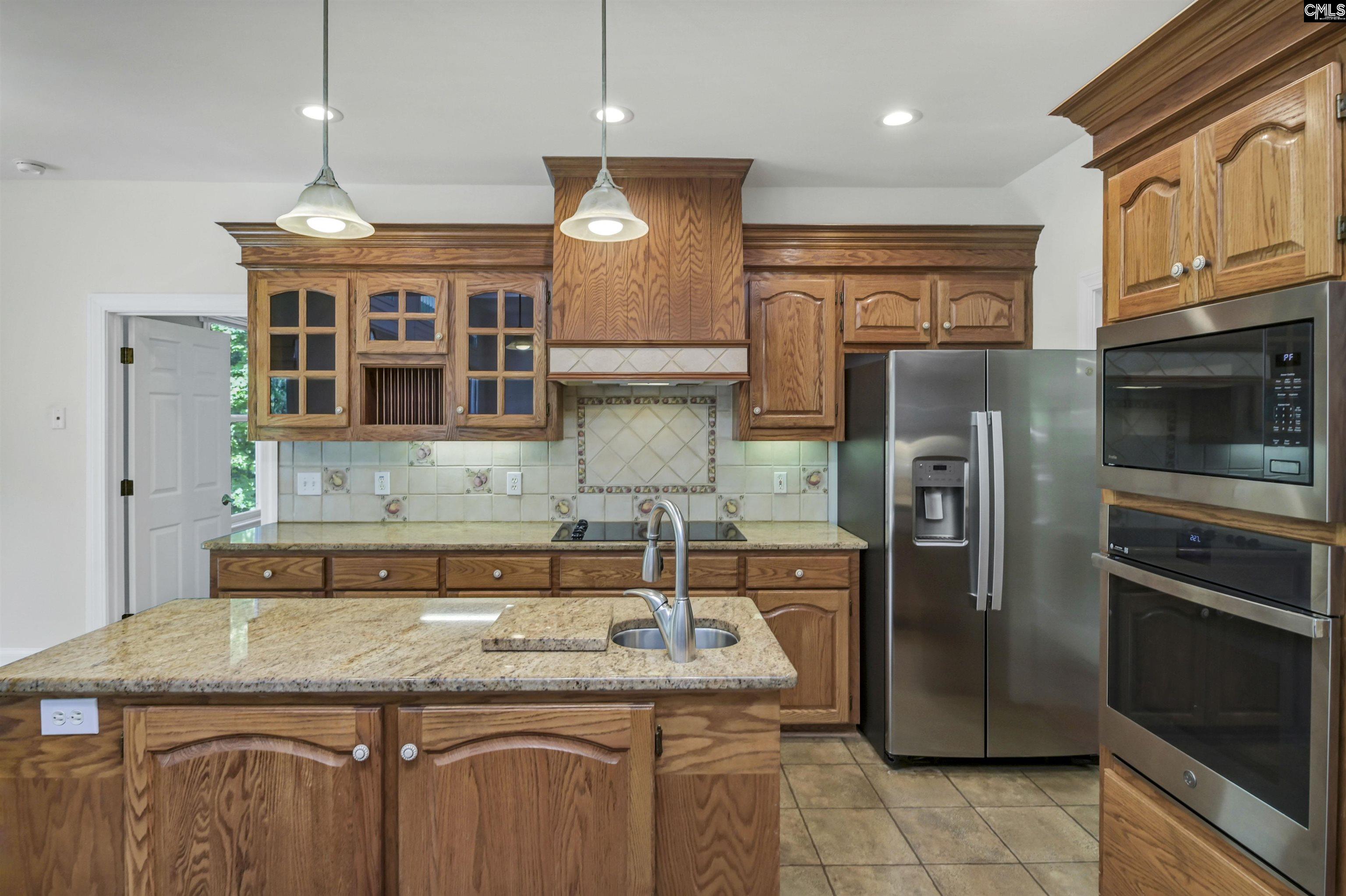 Kitchen with oak cabinets, granite island, stainless steel refrigerator, and built-in microwave and oven.