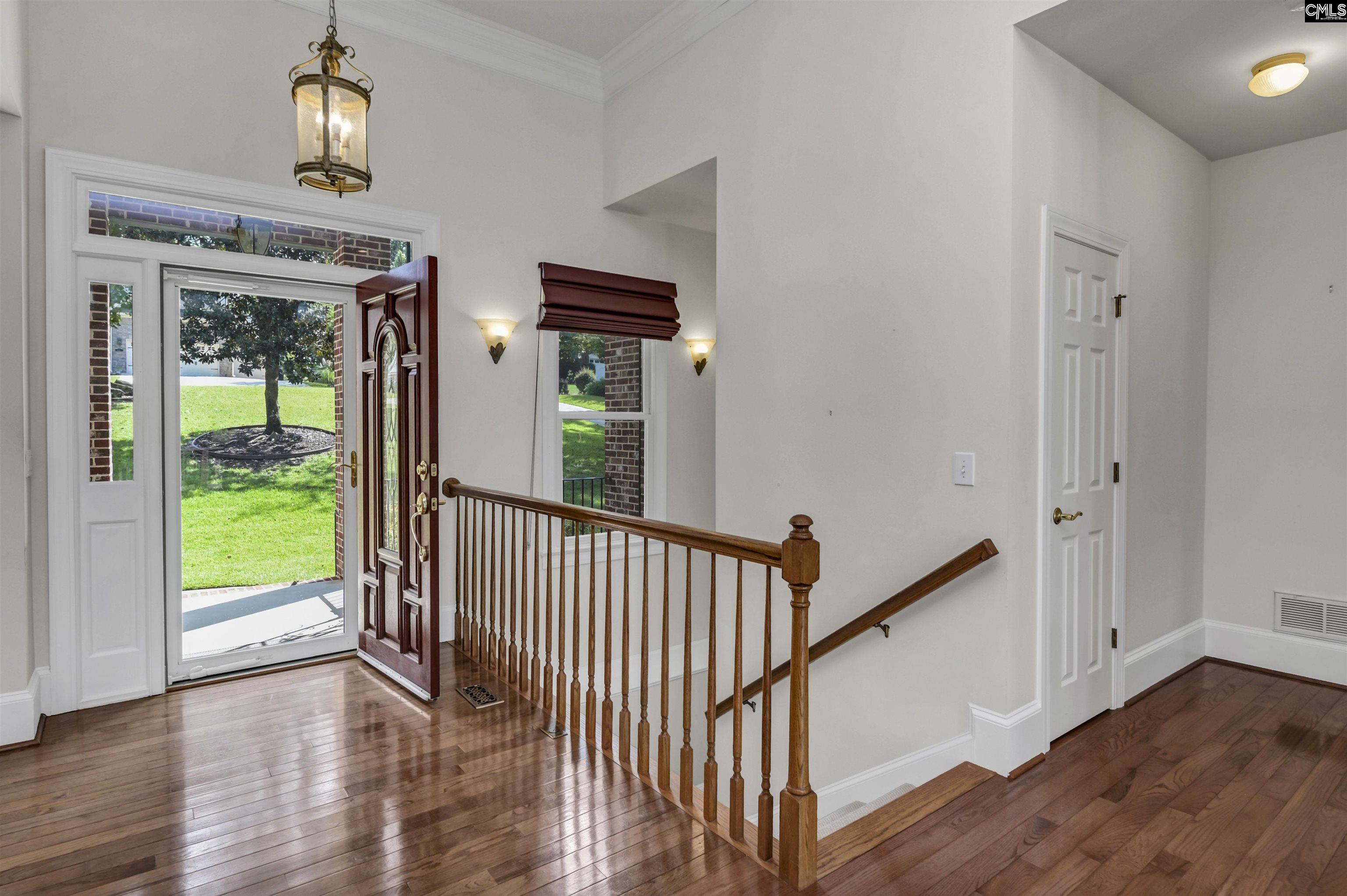 Entry foyer with hardwood floors, an open front door, and a wooden staircase railing.