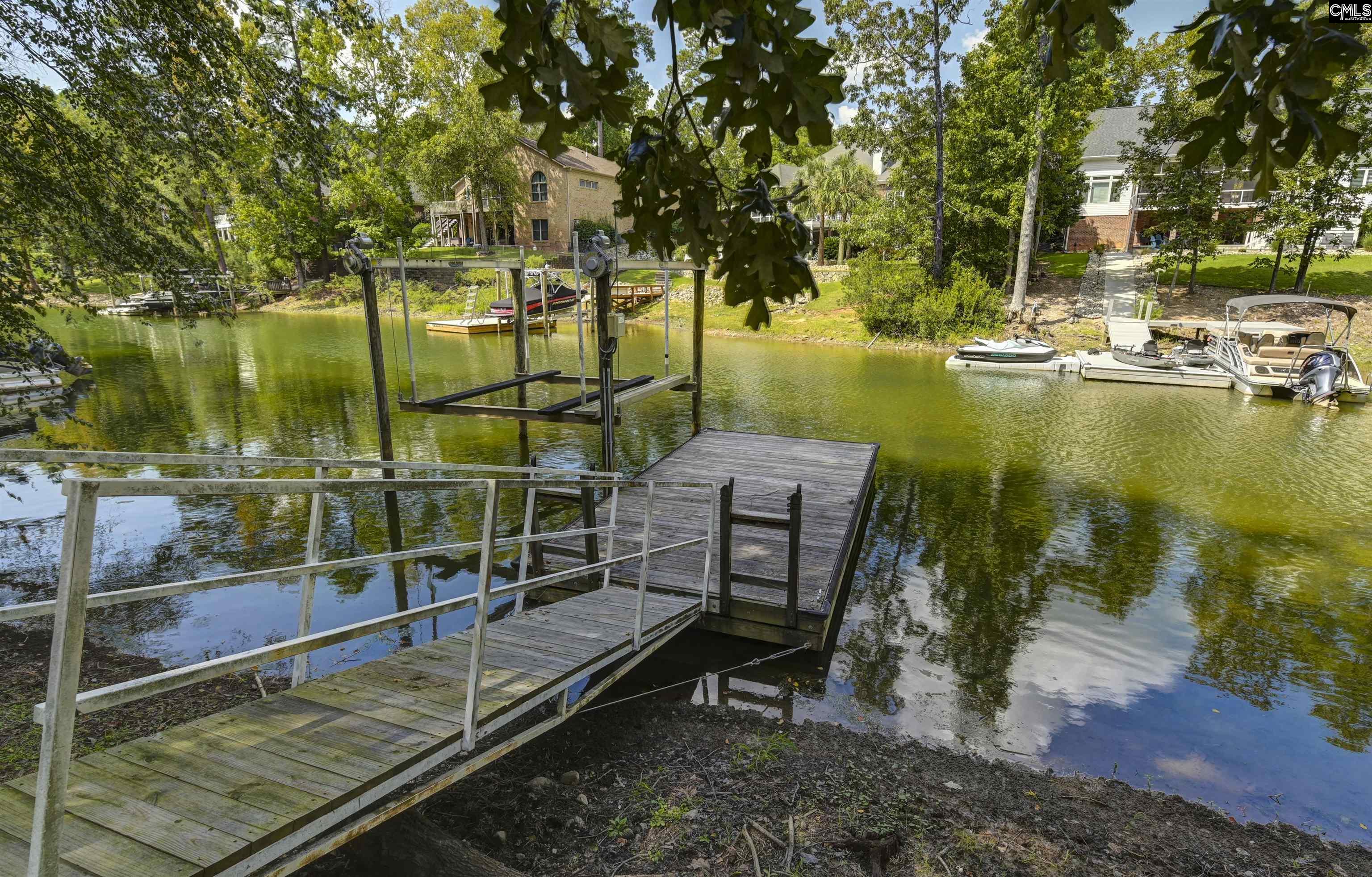 Wooden dock and gangway on a tree-lined lake, with a boat lift and boats across the cove.