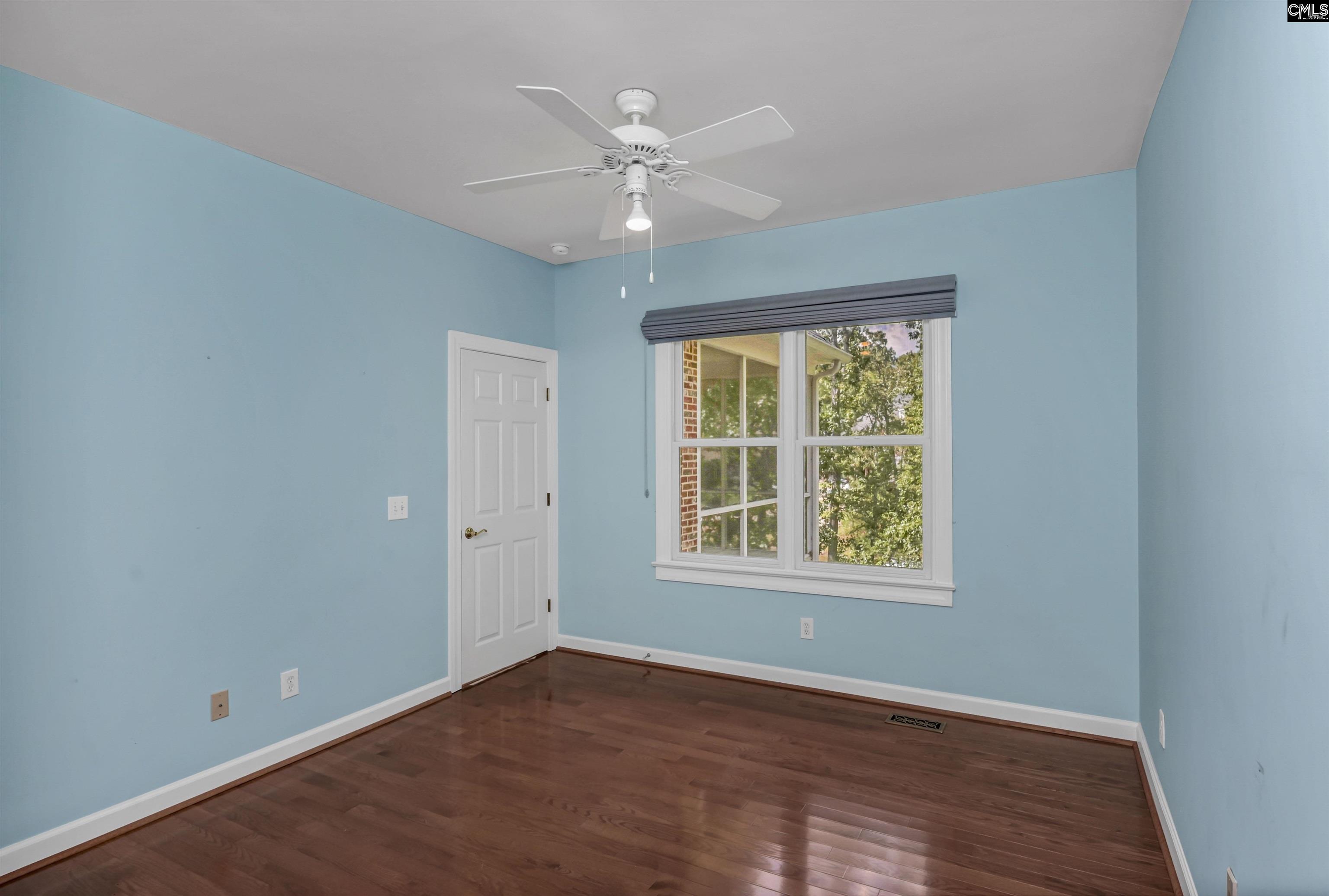 Empty room with blue walls, hardwood floors, a ceiling fan, and a large window.