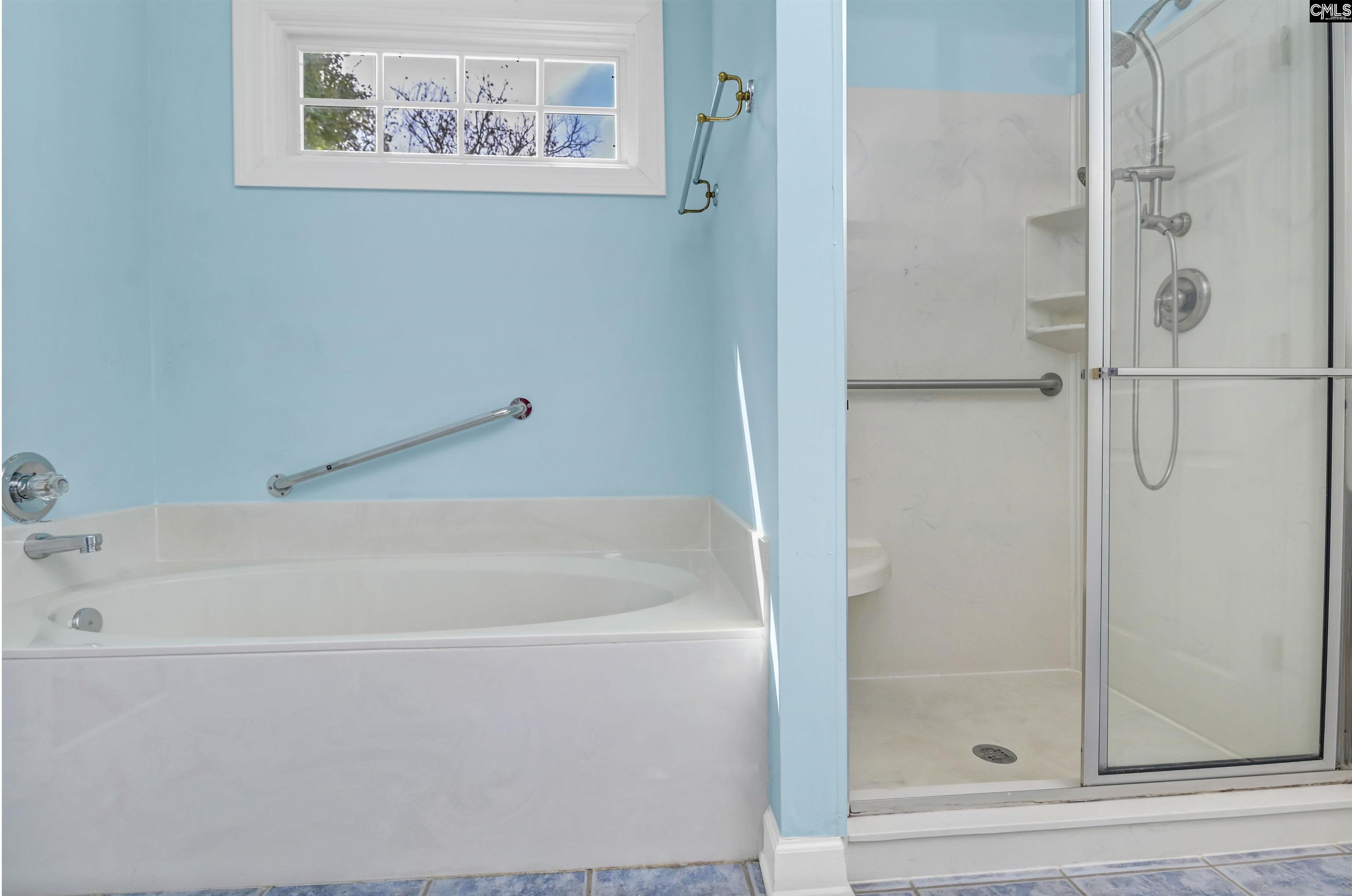 Bathroom with a white soaking tub, glass-enclosed shower, and light blue walls.