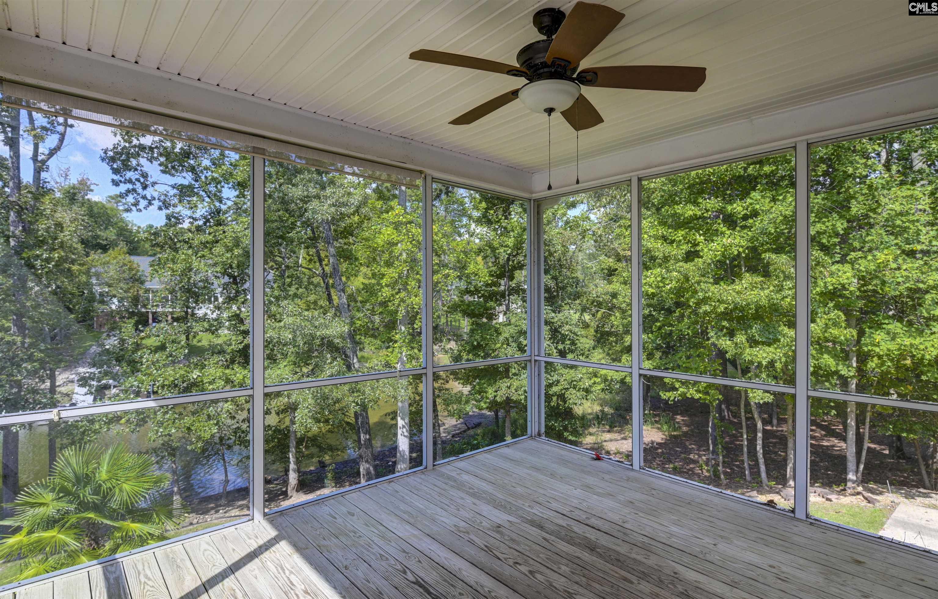 Screened-in porch with a ceiling fan and wooded views through the screens.