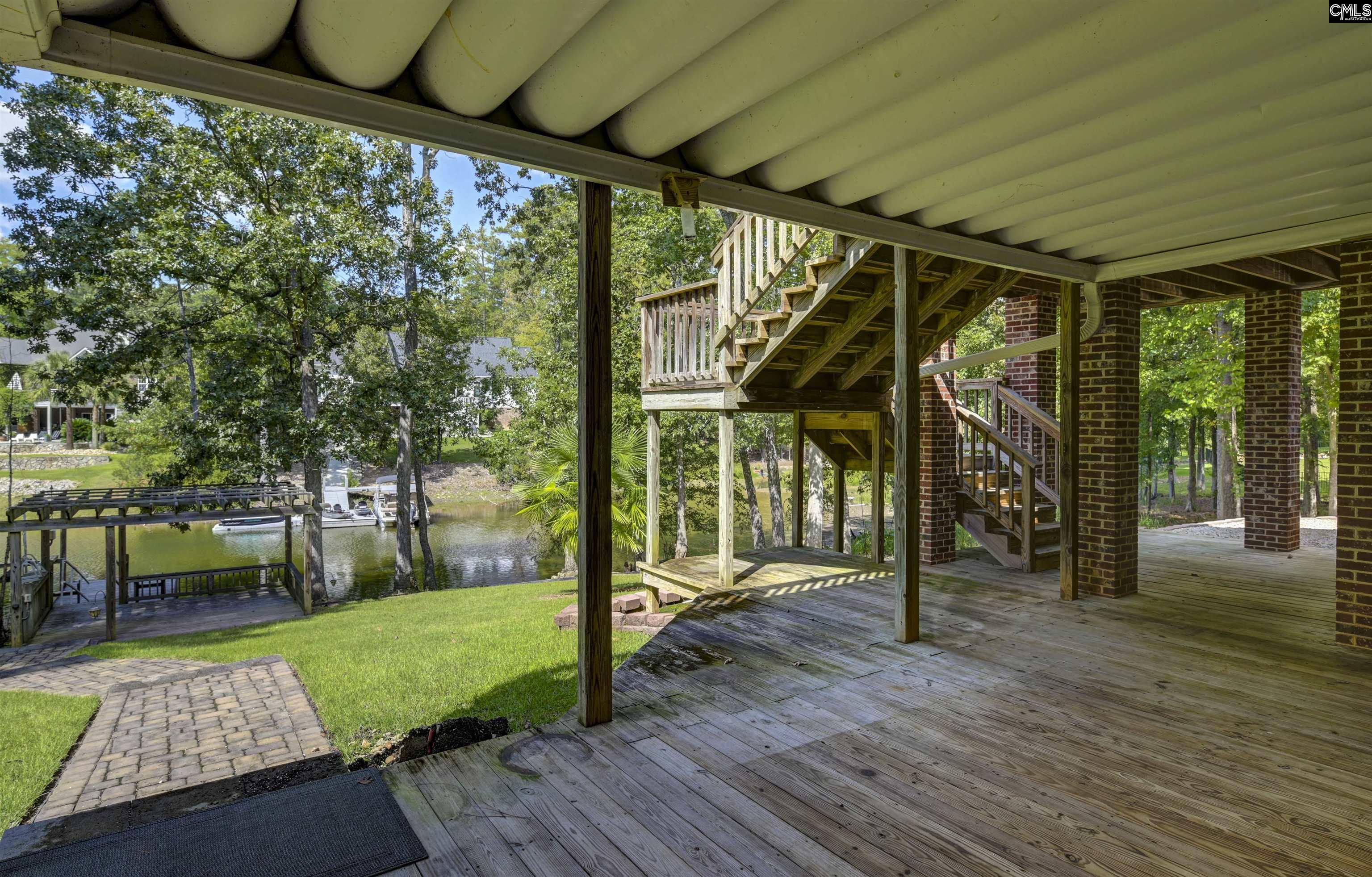 Covered waterfront deck with wooden stairs, a grassy yard, and a dock beside the water.