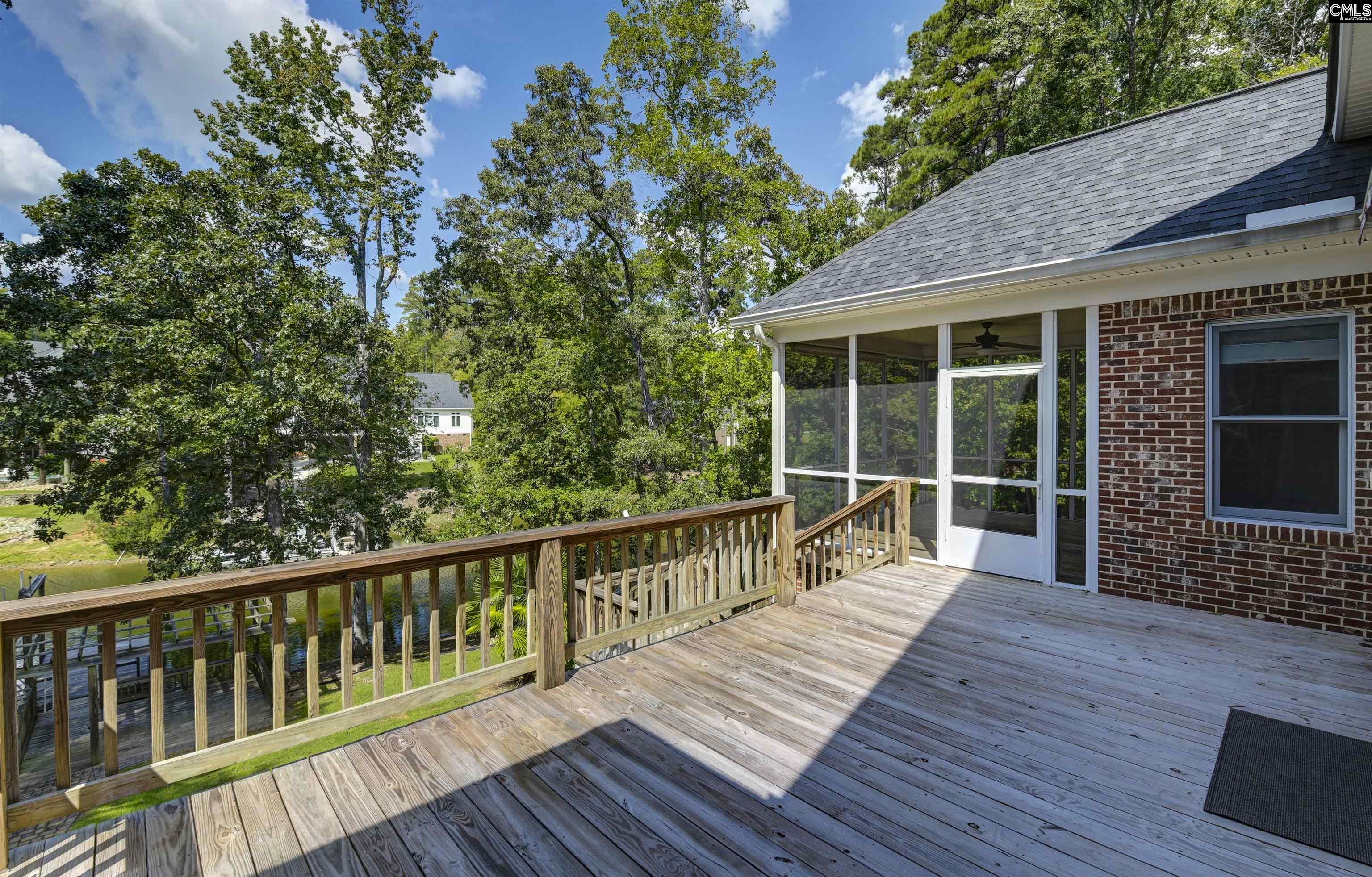 Elevated wood deck beside a screened porch, overlooking leafy trees and a glimpse of water.