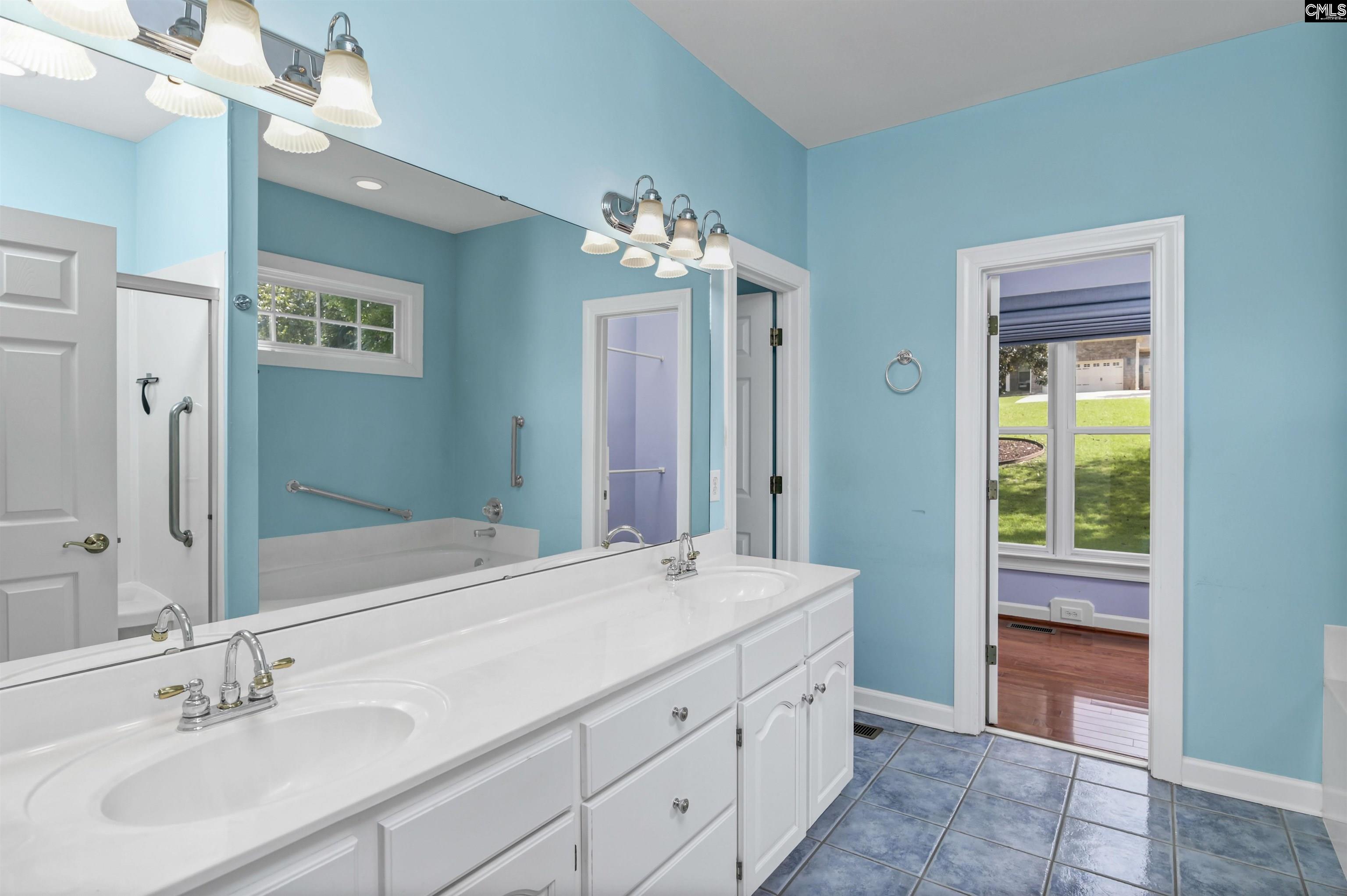 Bathroom with a double-sink vanity, turquoise walls, blue tile floor, and grab bars beside the tub.