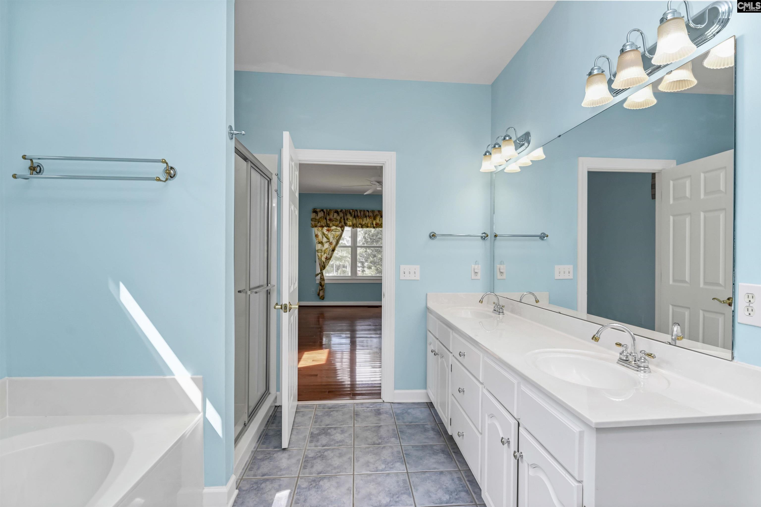 Bathroom with turquoise walls, a long white double vanity, tiled floor, and bathtub beside a glass shower.