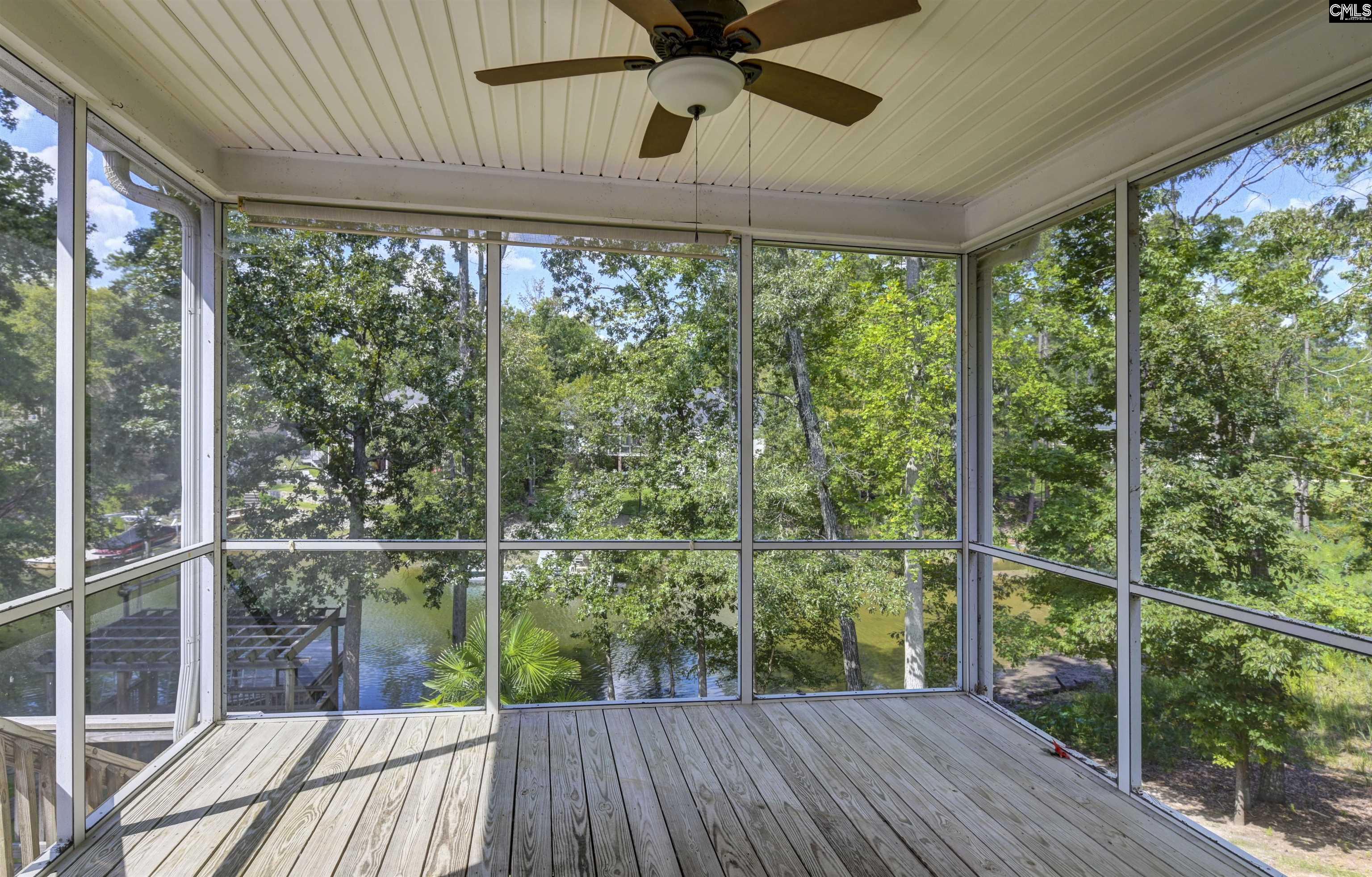 Screened porch overlooking a lake, with a ceiling fan and weathered wood-plank floor.