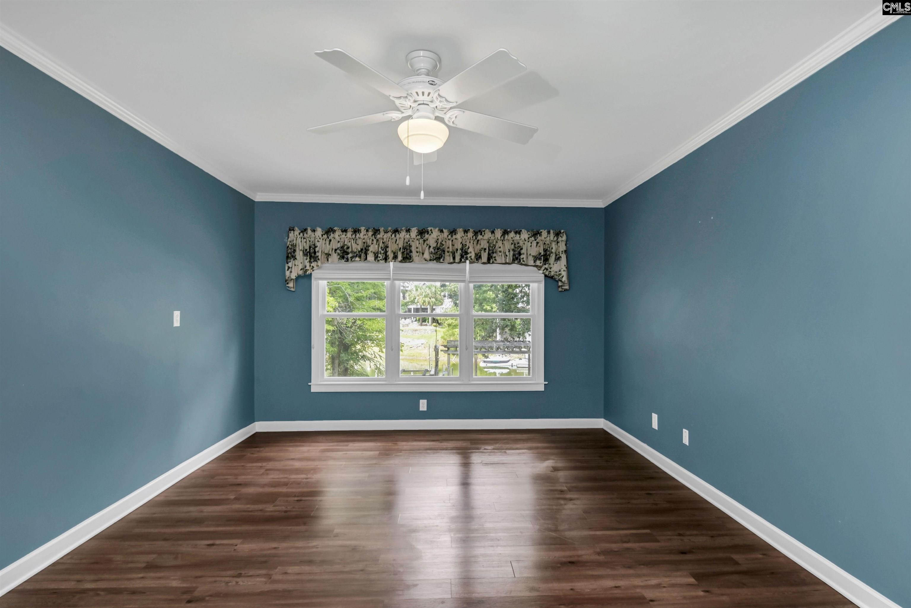 Empty teal bedroom with dark wood floors, a ceiling fan, and a wide window overlooking greenery.
