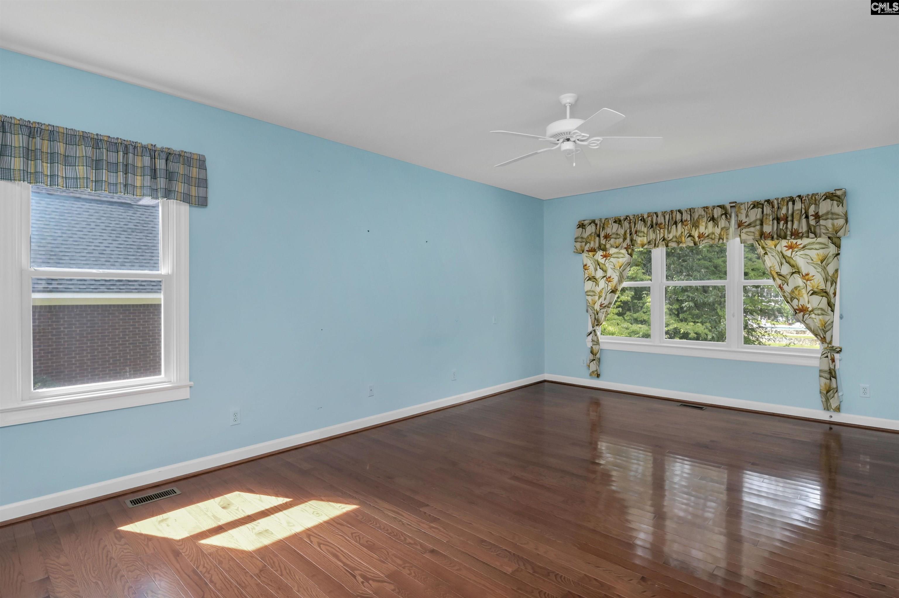 Empty bedroom with blue walls, polished hardwood floors, and two curtained windows.
