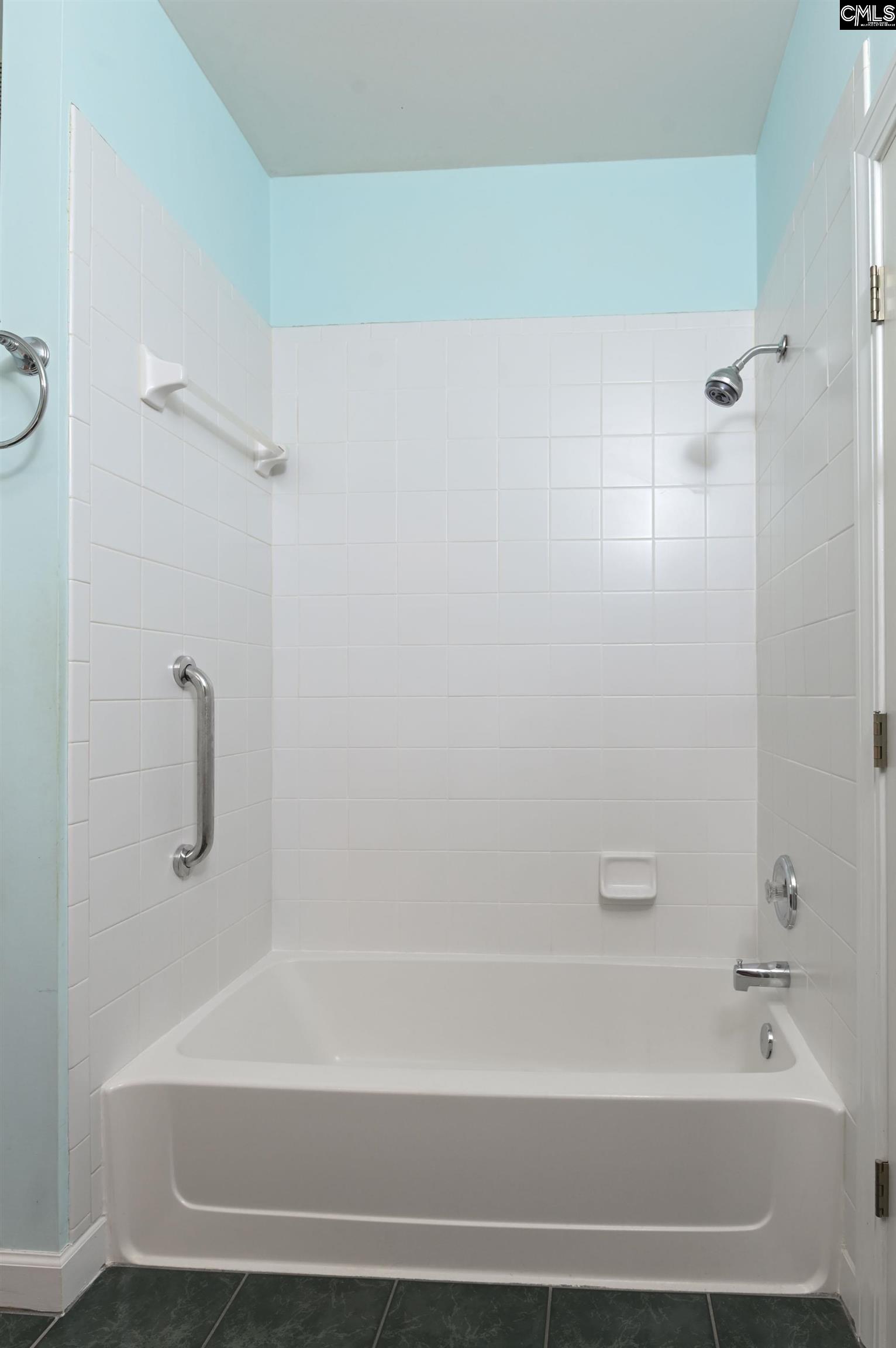 Bathroom with a white tiled tub and shower, chrome fixtures, and grab bars.