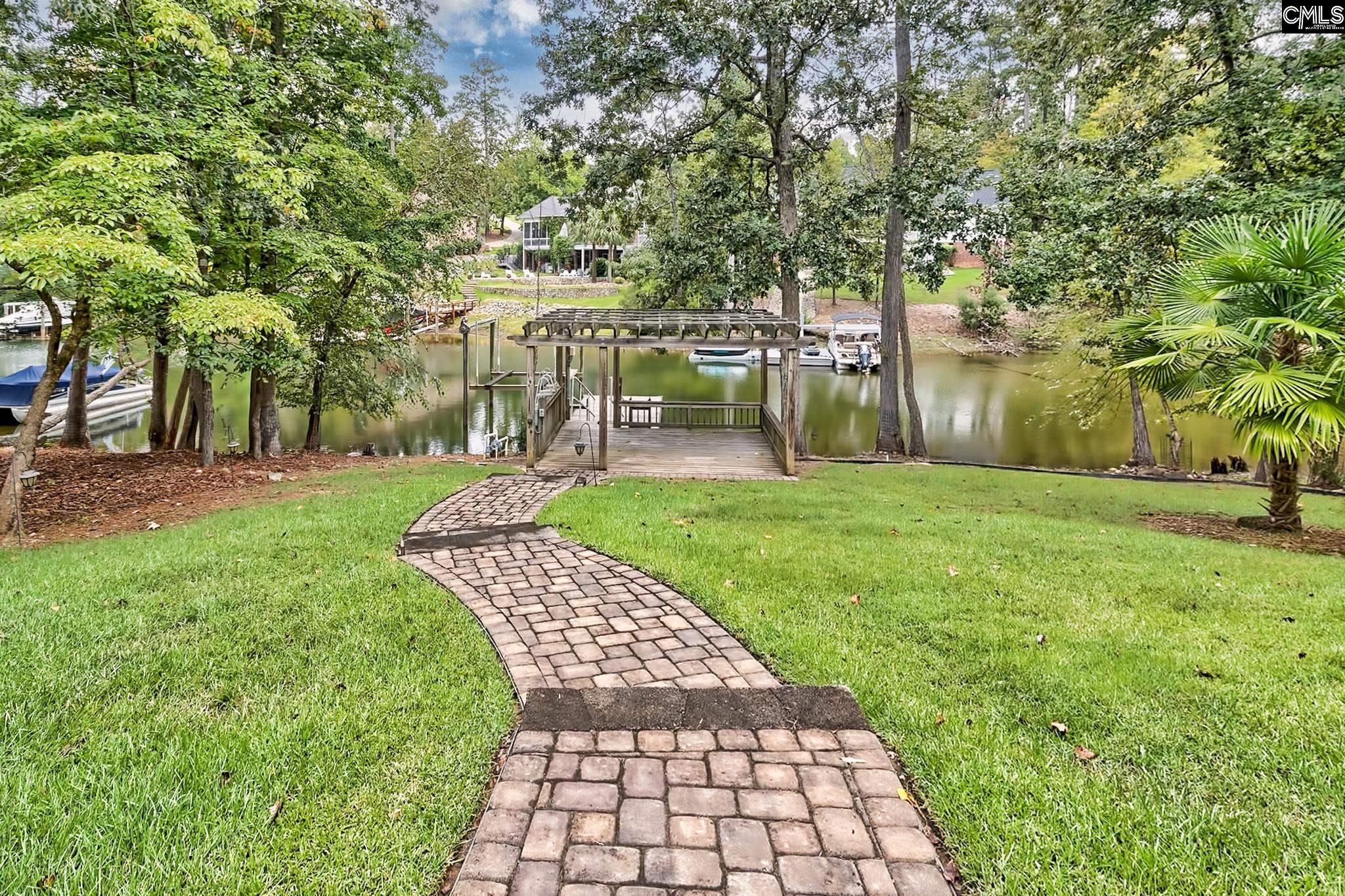 Waterfront lawn and paver path leading to a private dock, with boats on the water.