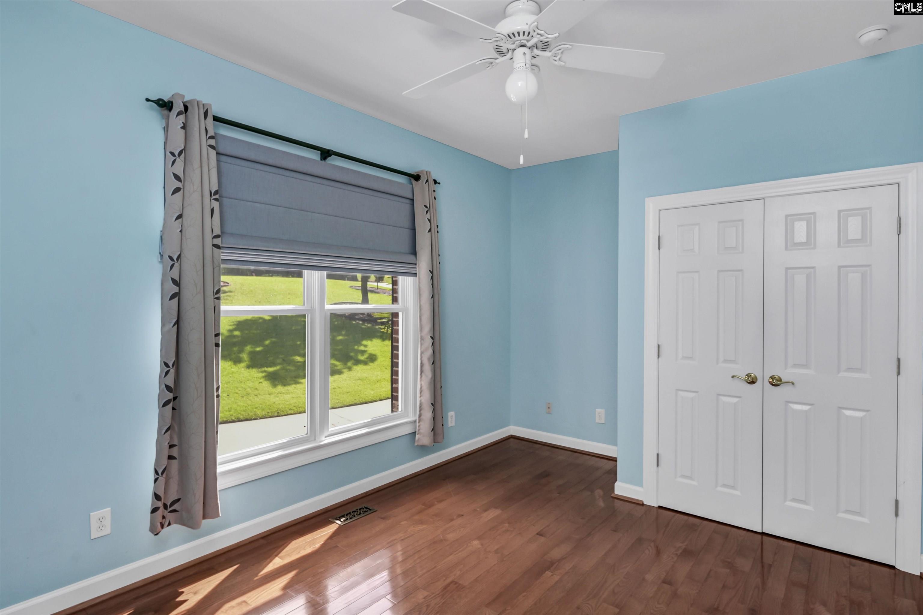 Empty blue room with hardwood floors, curtained window, and white double closet doors.