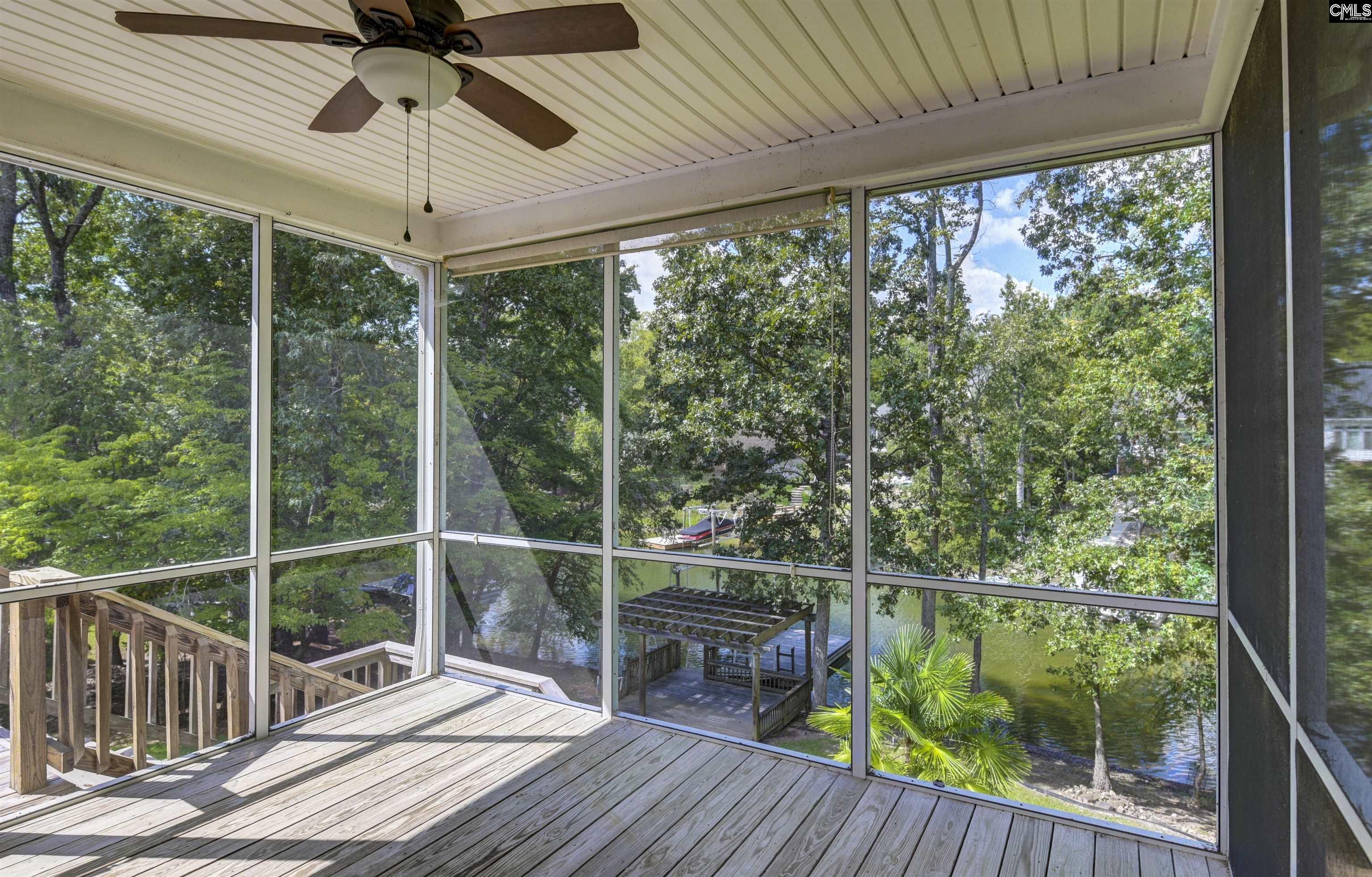Screened-in porch overlooking a wooded waterfront, with a dock and boat below.