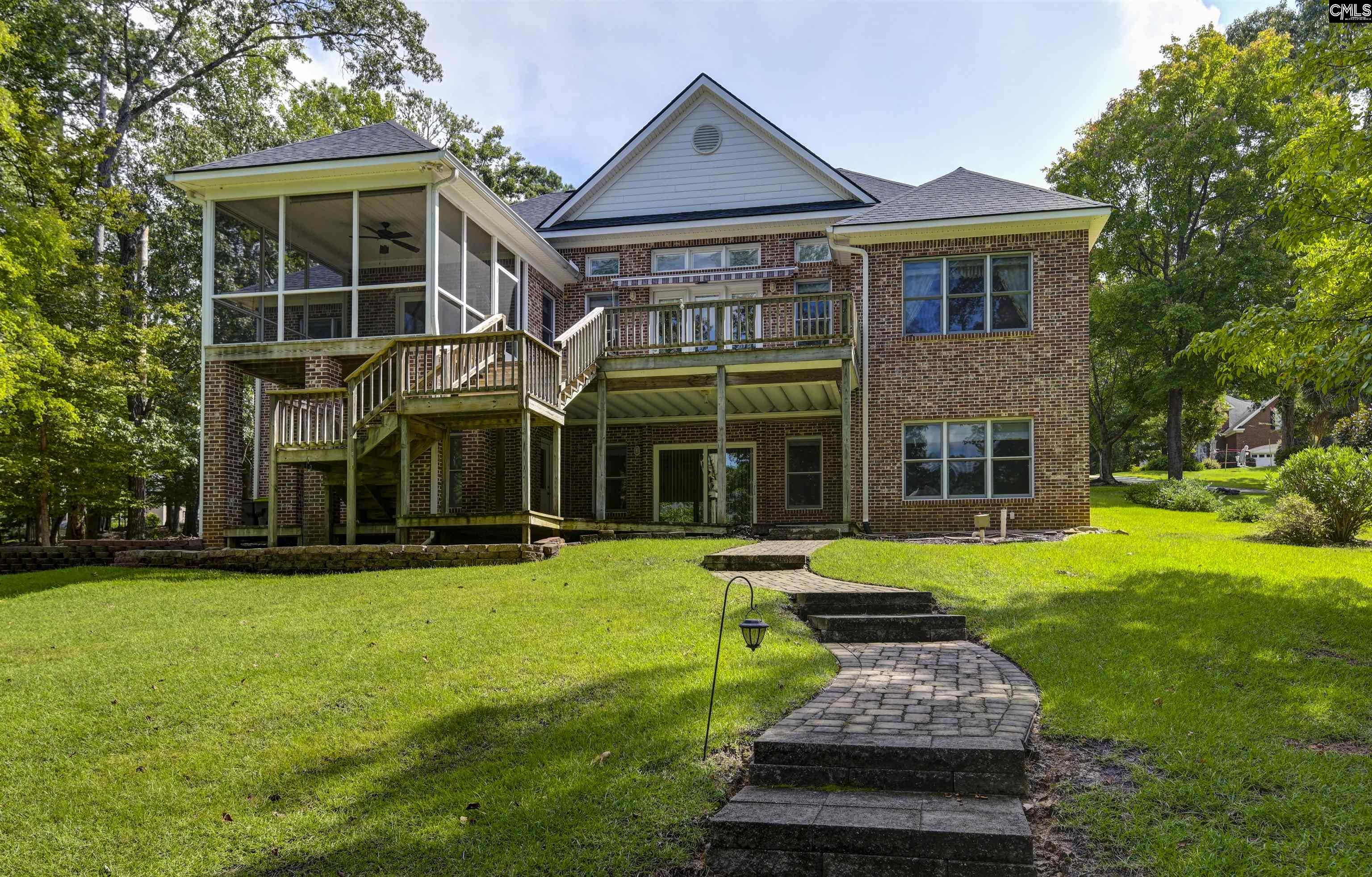 Two-story brick house with a screened porch, elevated decks, and a curved stone path across the lawn.