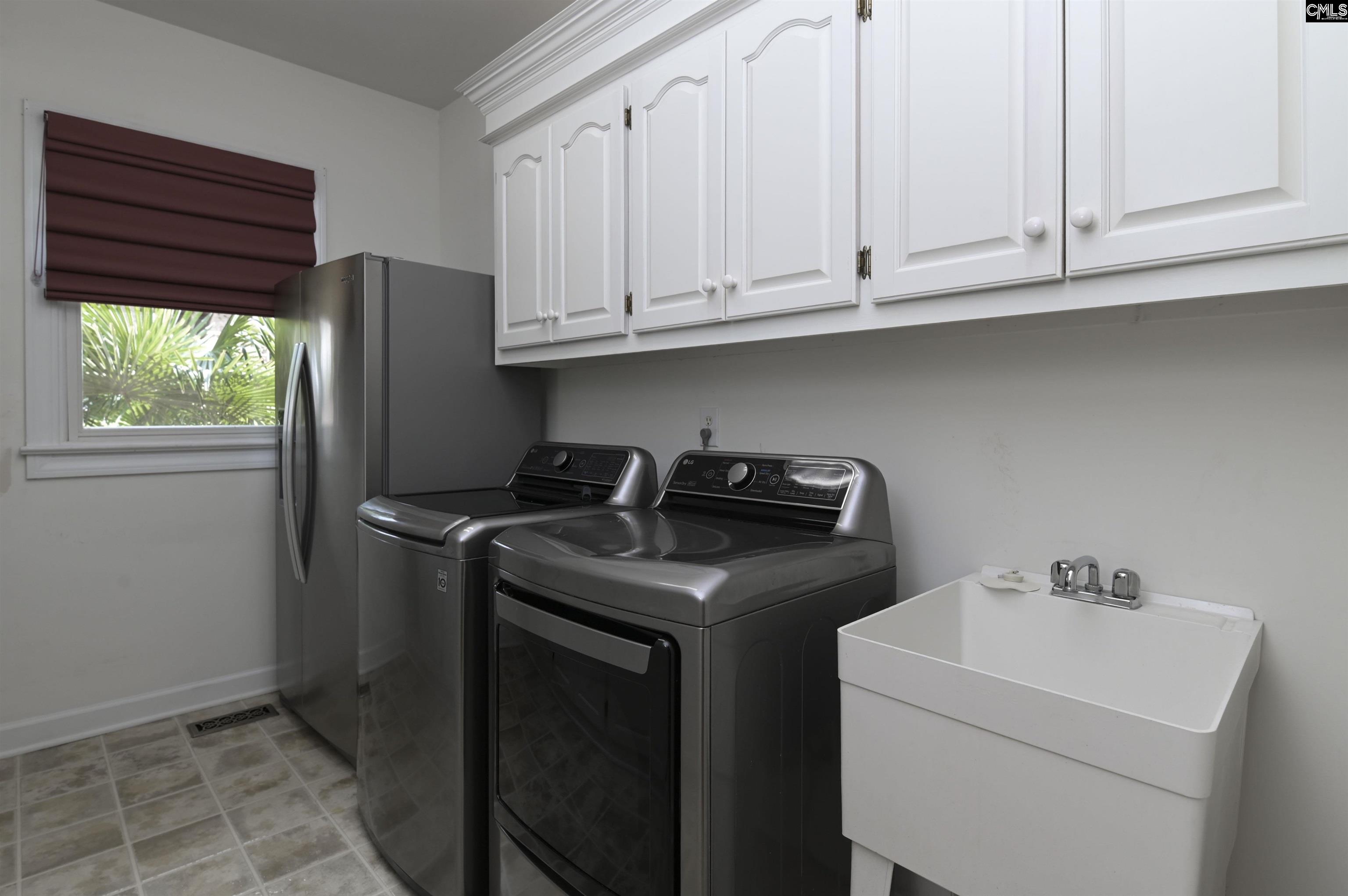 Laundry room with washer, dryer, deep utility sink, and white cabinets.