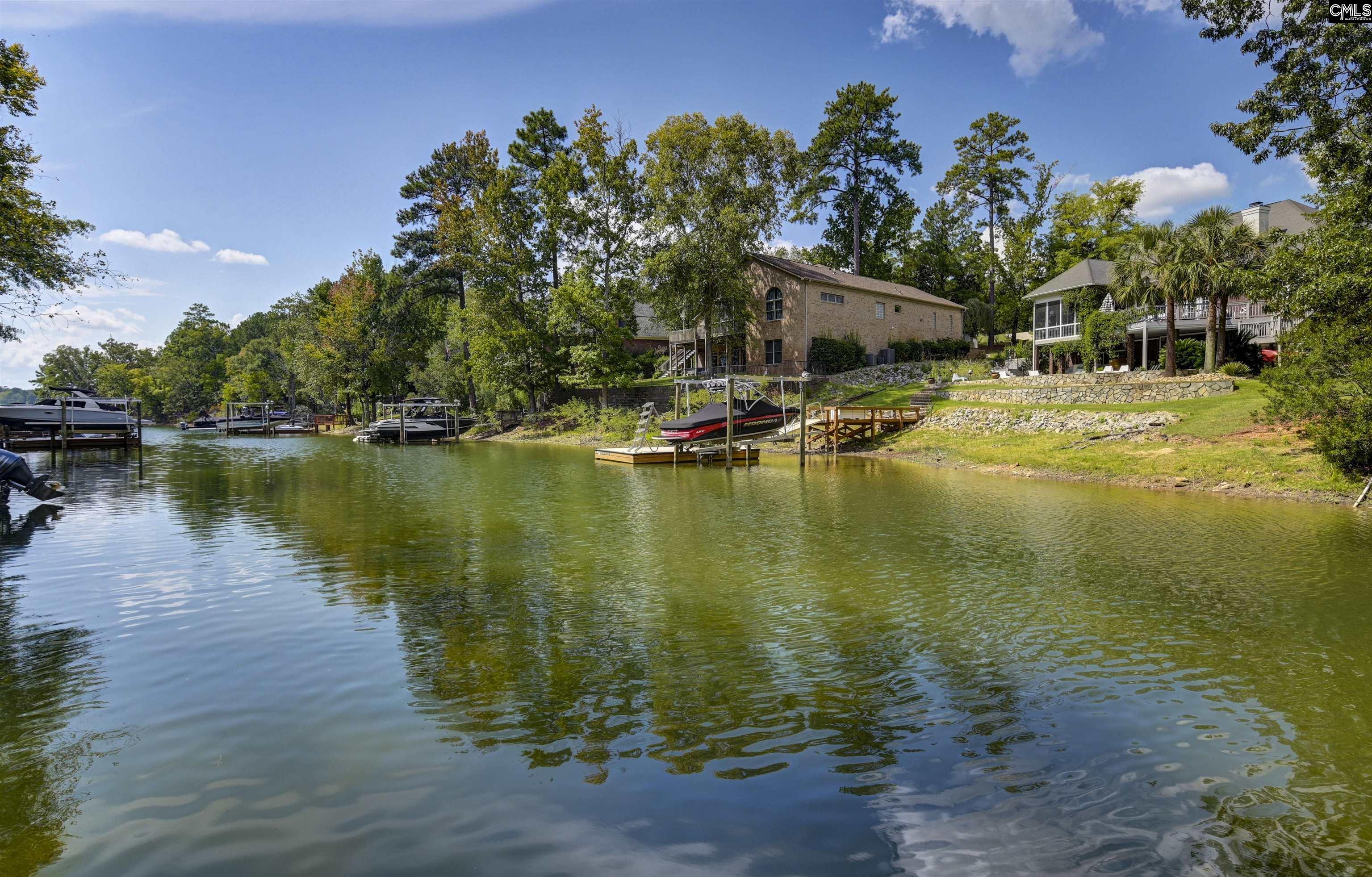 Waterfront homes and private docks line a tree-shaded lake with boats moored along the shore.