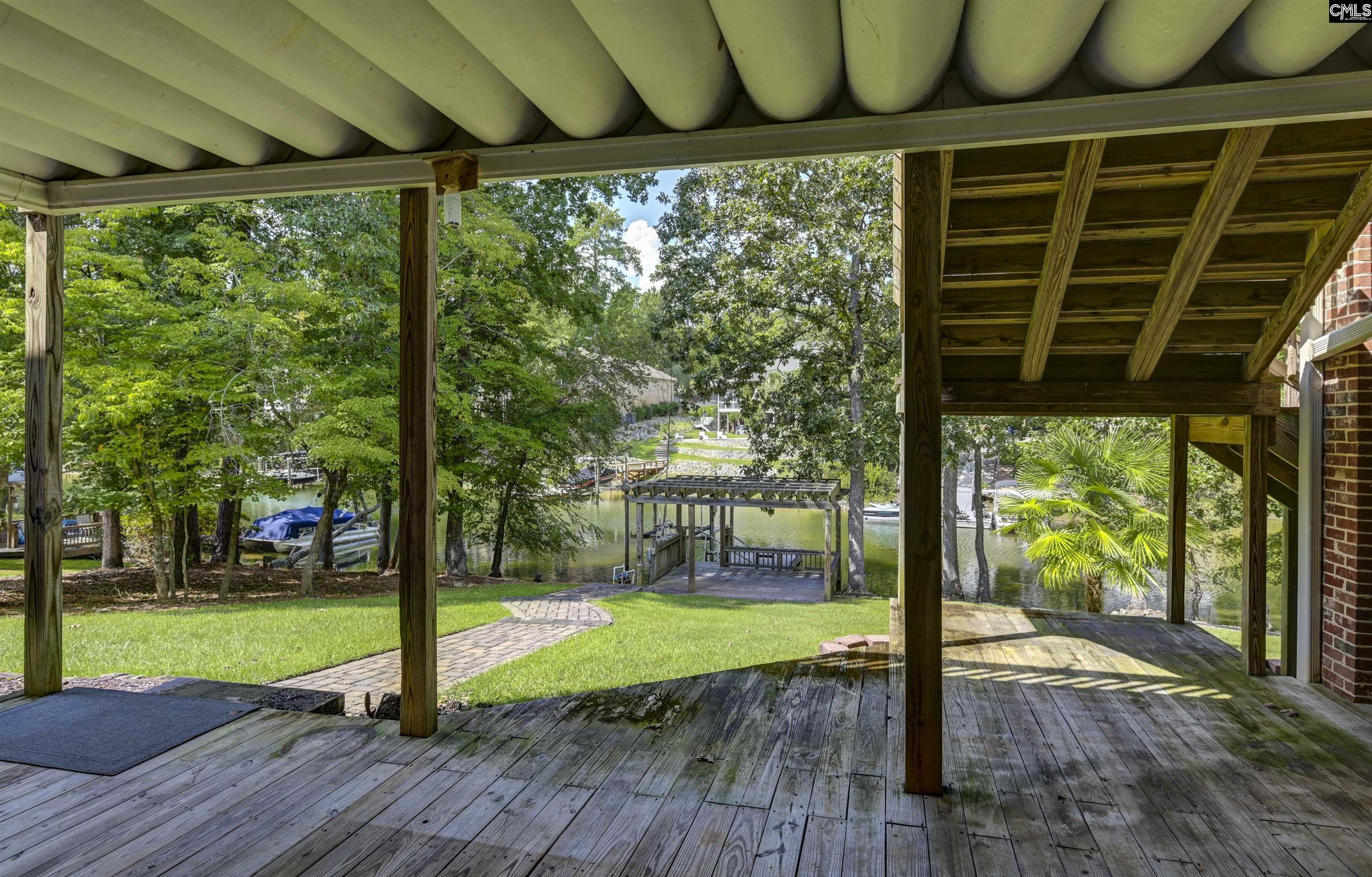 Covered rear deck overlooks a wooded lakefront, dock, and boats.