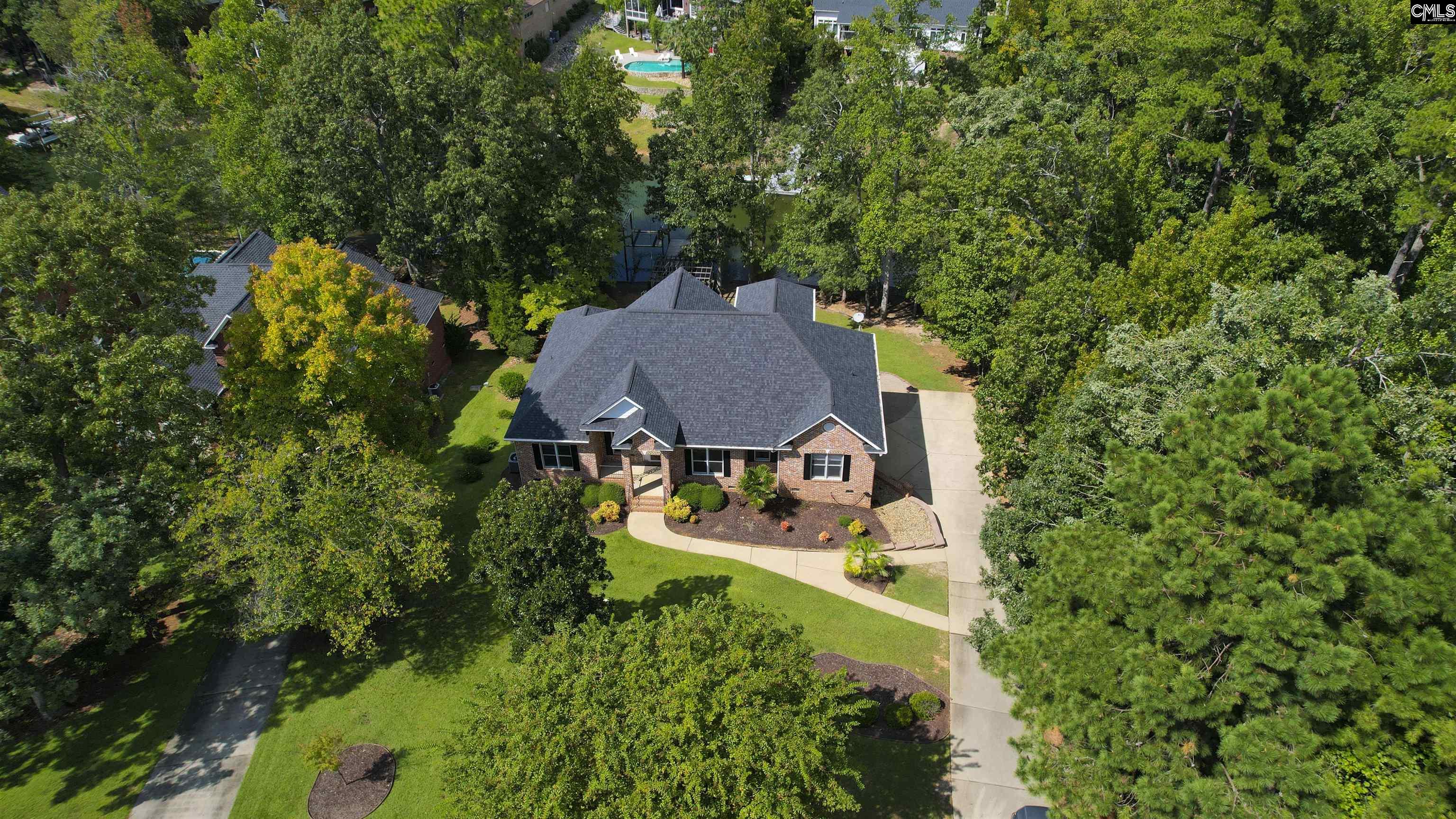 Aerial view of a brick home surrounded by mature trees, with a landscaped lawn and long driveway.