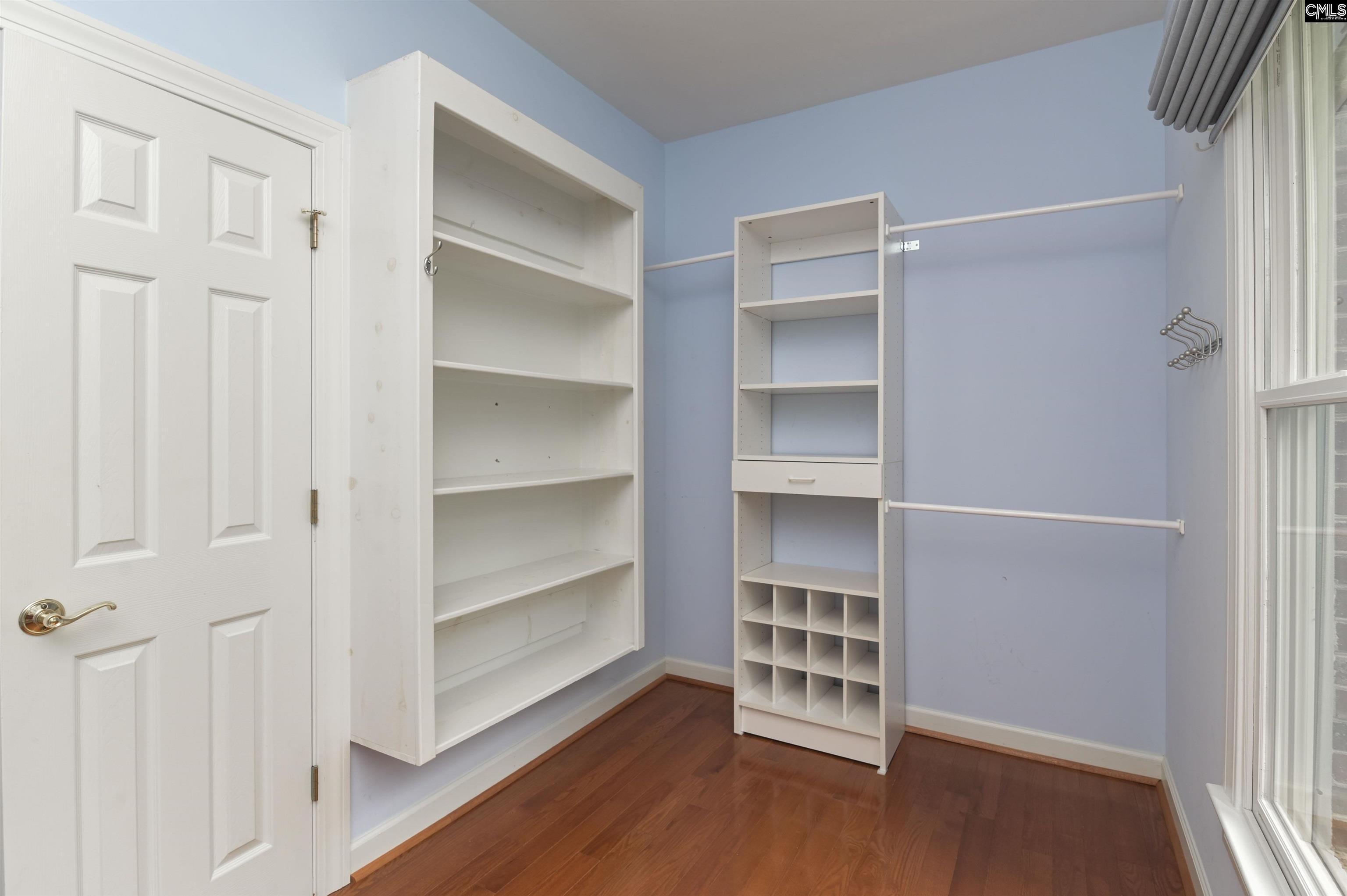 Walk-in closet with white shelving, hanging rods, shoe cubbies, and a large window.
