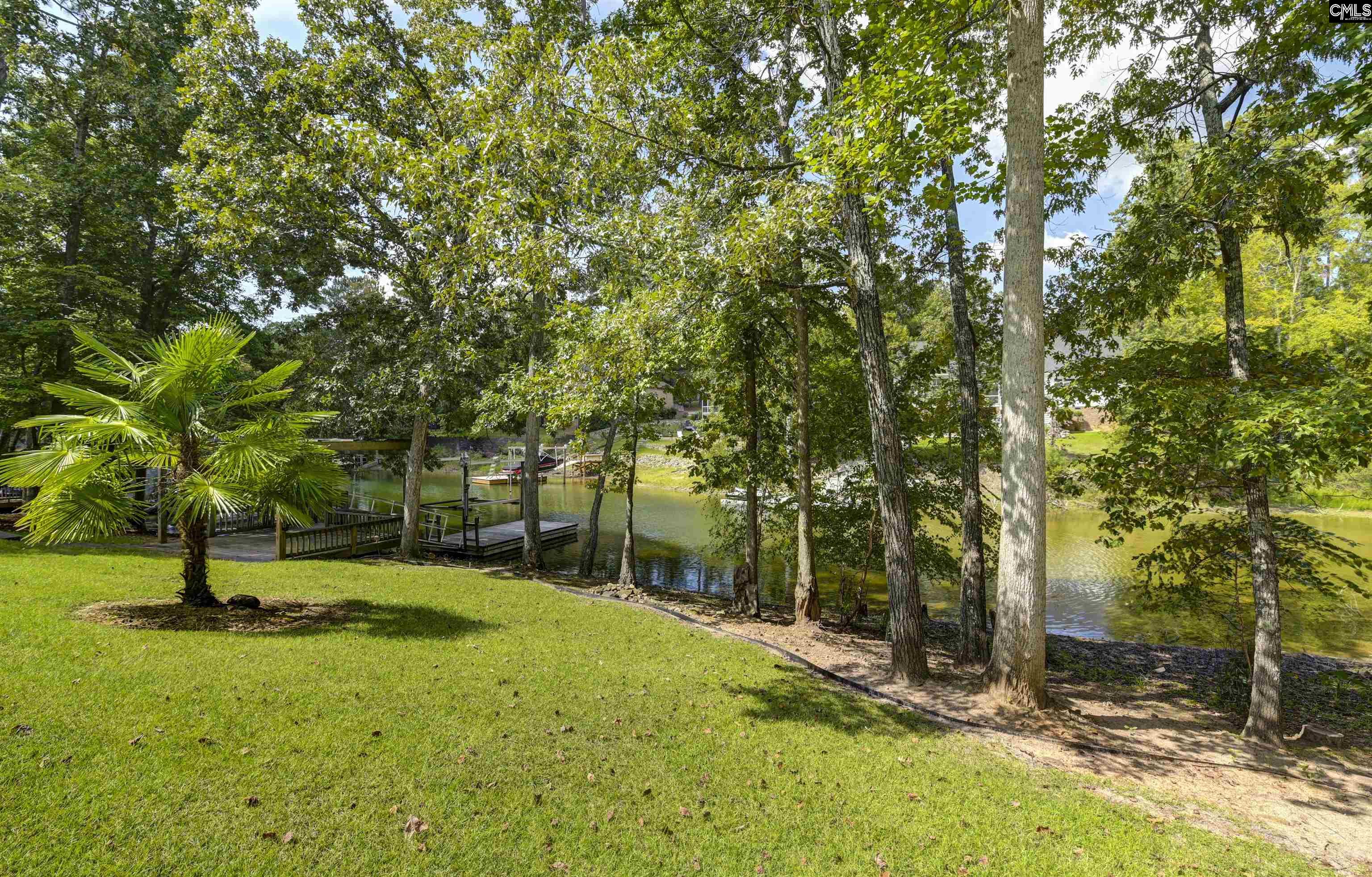 Waterfront yard with mature trees, a palm, and docks along a calm lake.