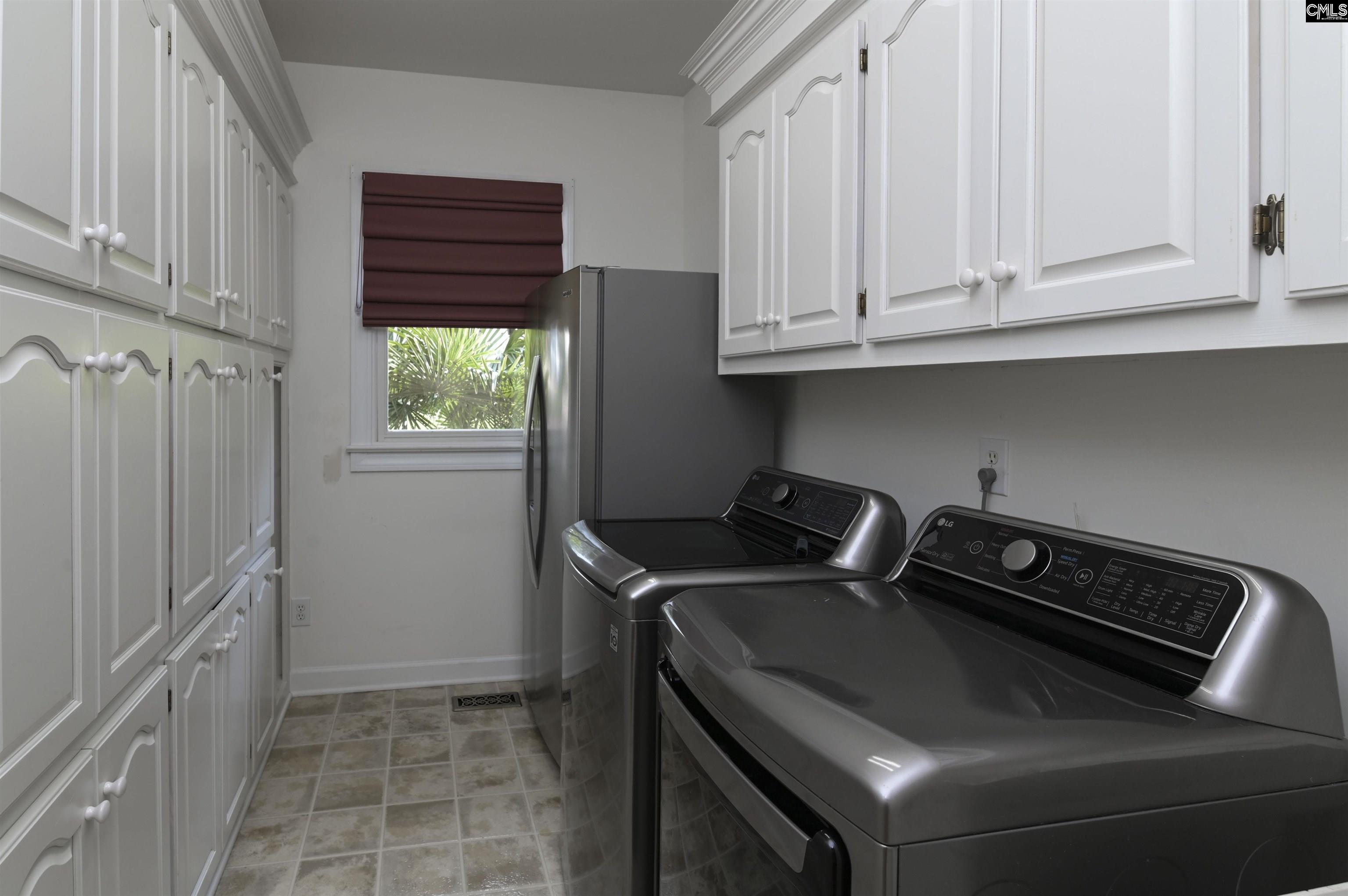 Laundry room with white built-in cabinets, dark gray washer and dryer, and a window with a burgundy shade.