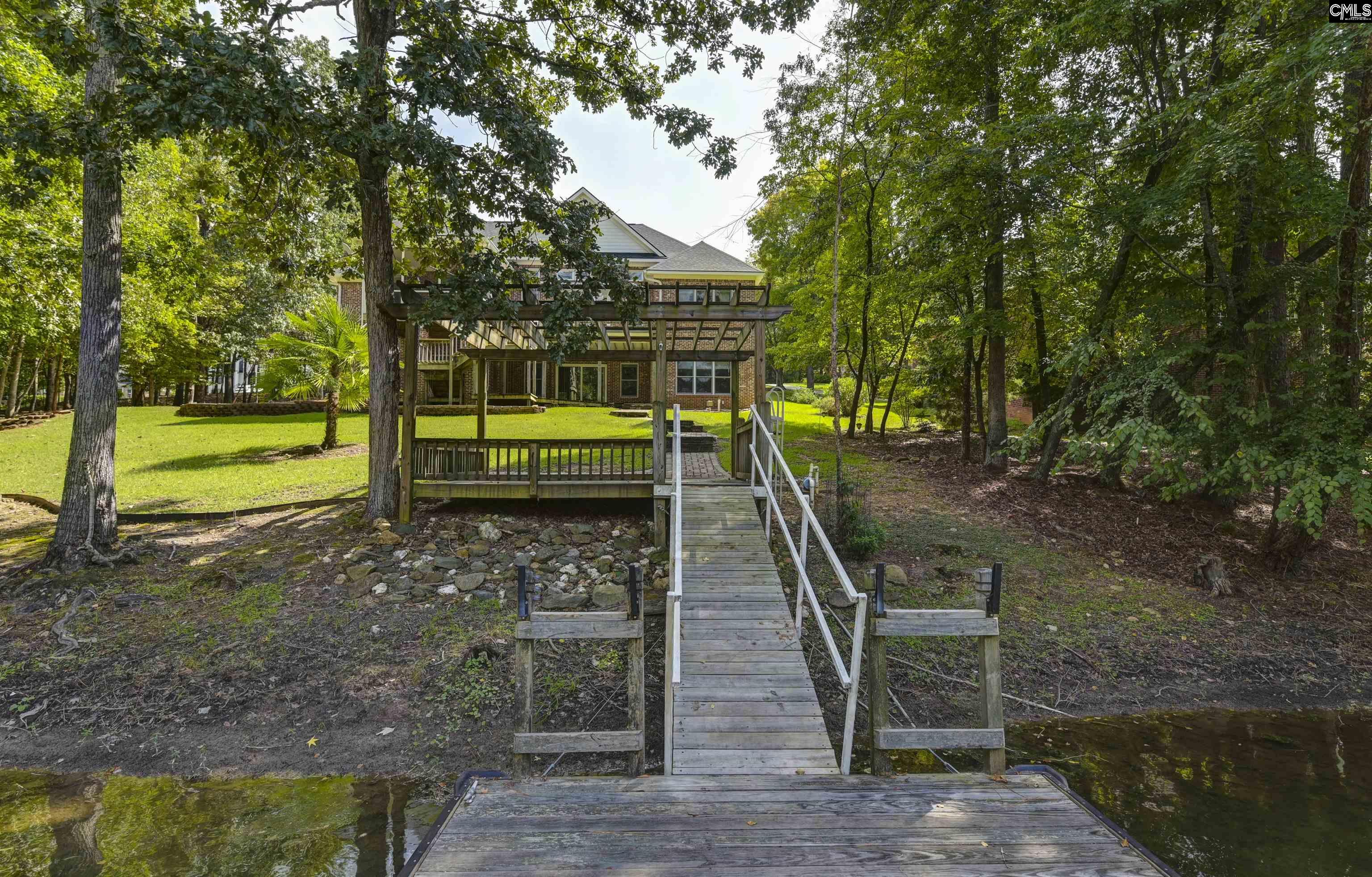 Brick home with a covered deck, reached by a wooden dock through a wooded waterfront yard.