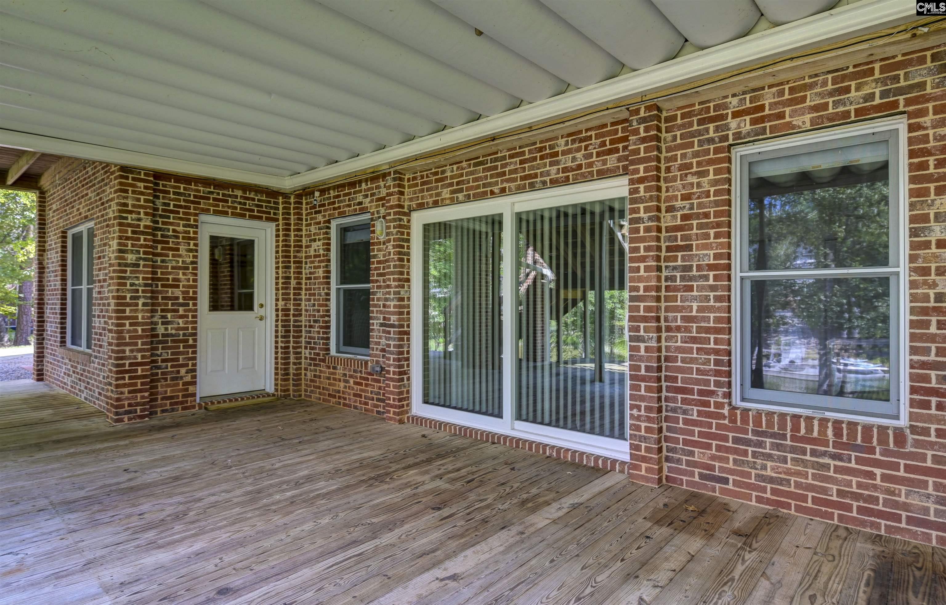 Covered wooden deck beside a red-brick wall, with sliding glass doors and a white ceiling.