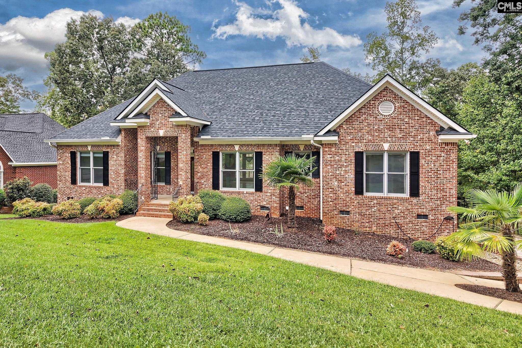 Red brick home with black shutters, landscaped garden beds, and a broad green lawn.