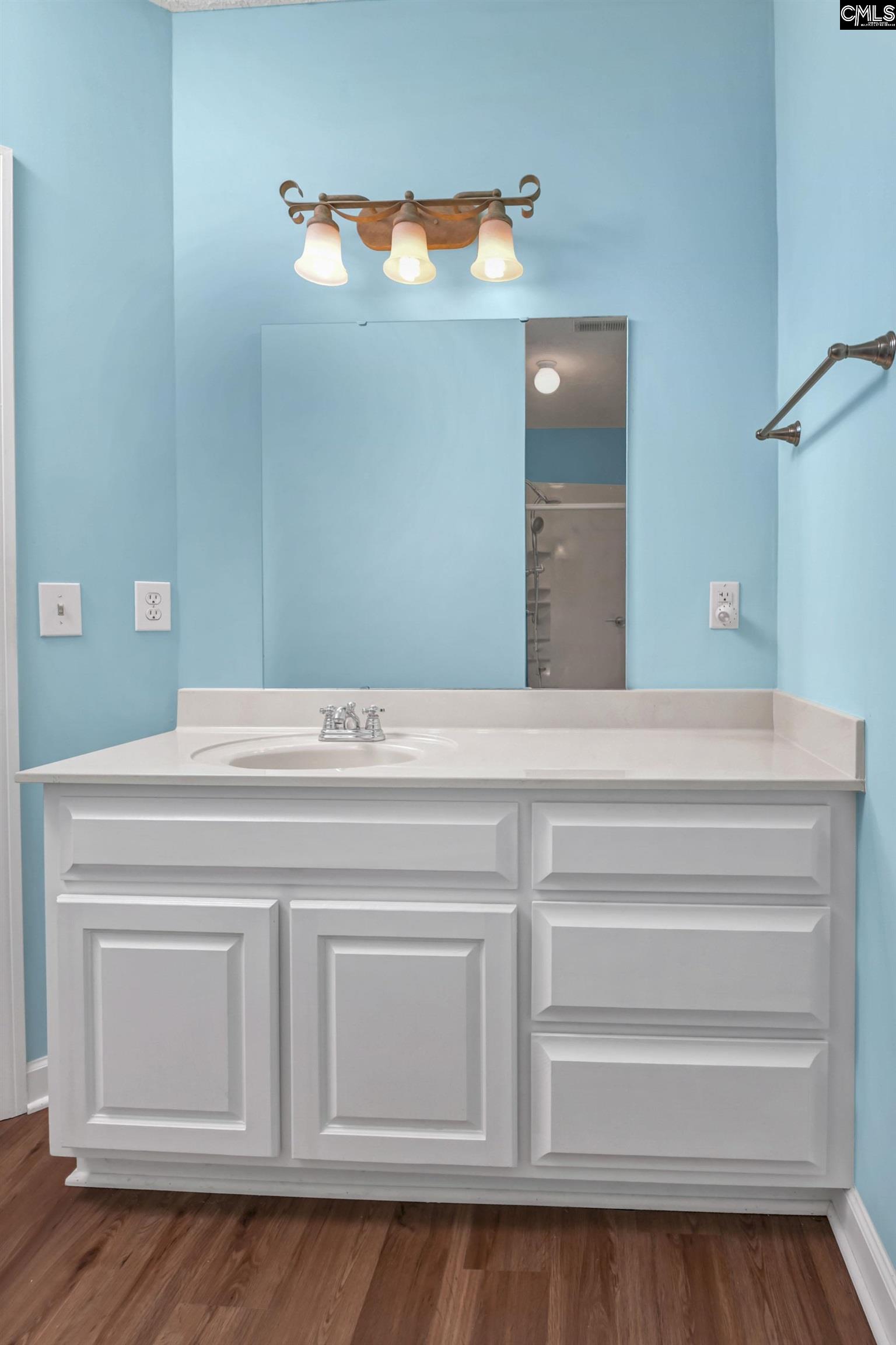 Bathroom vanity with white paneled cabinets, a large mirror, and bright blue walls.