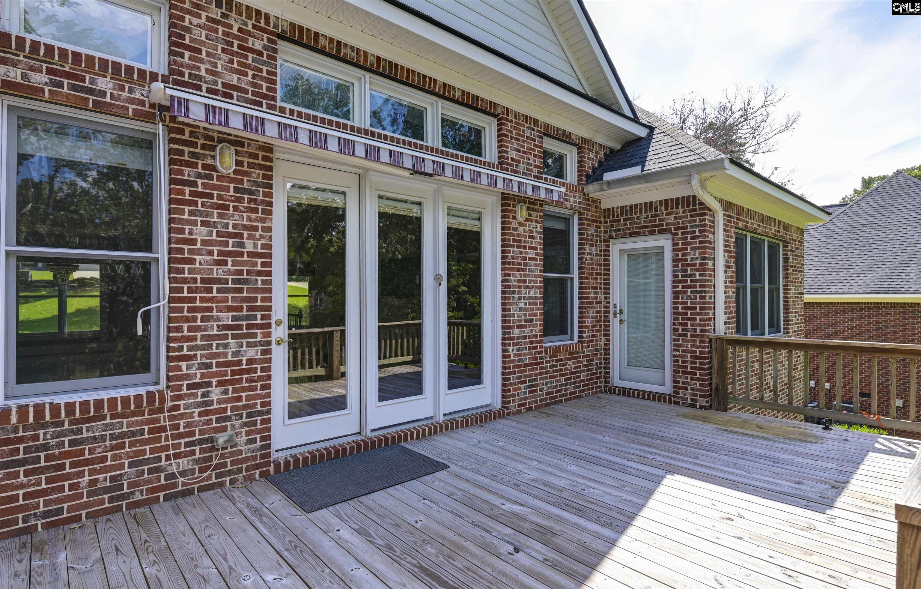 Red brick home exterior with glass doors, striped awning, and a broad wooden deck.