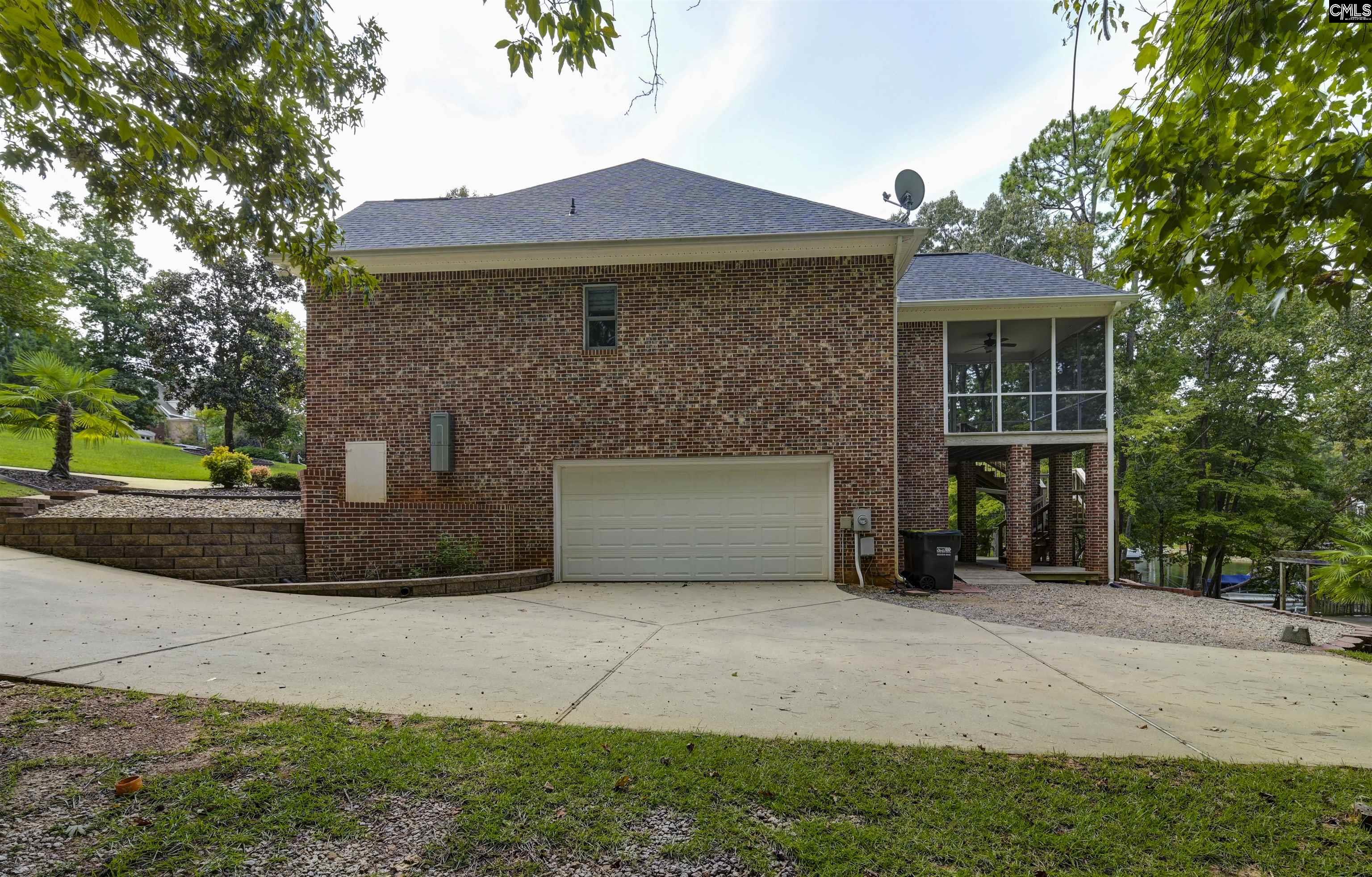 Brick home with a double garage and elevated screened porch, surrounded by trees with a glimpse of water.