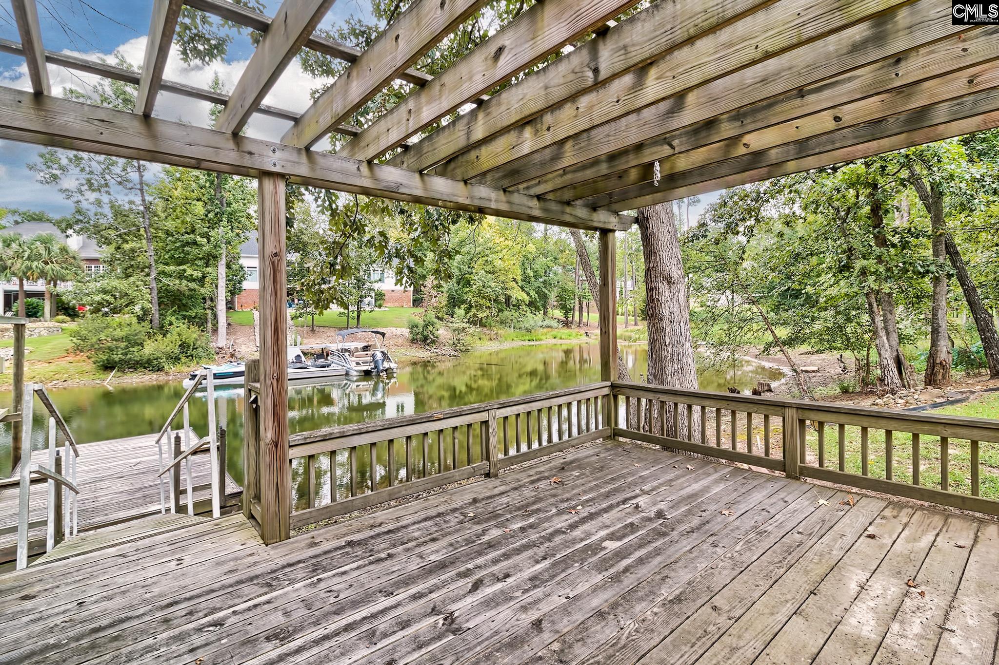 Wooden pergola deck overlooking a tree-lined waterway, dock, and moored boats.