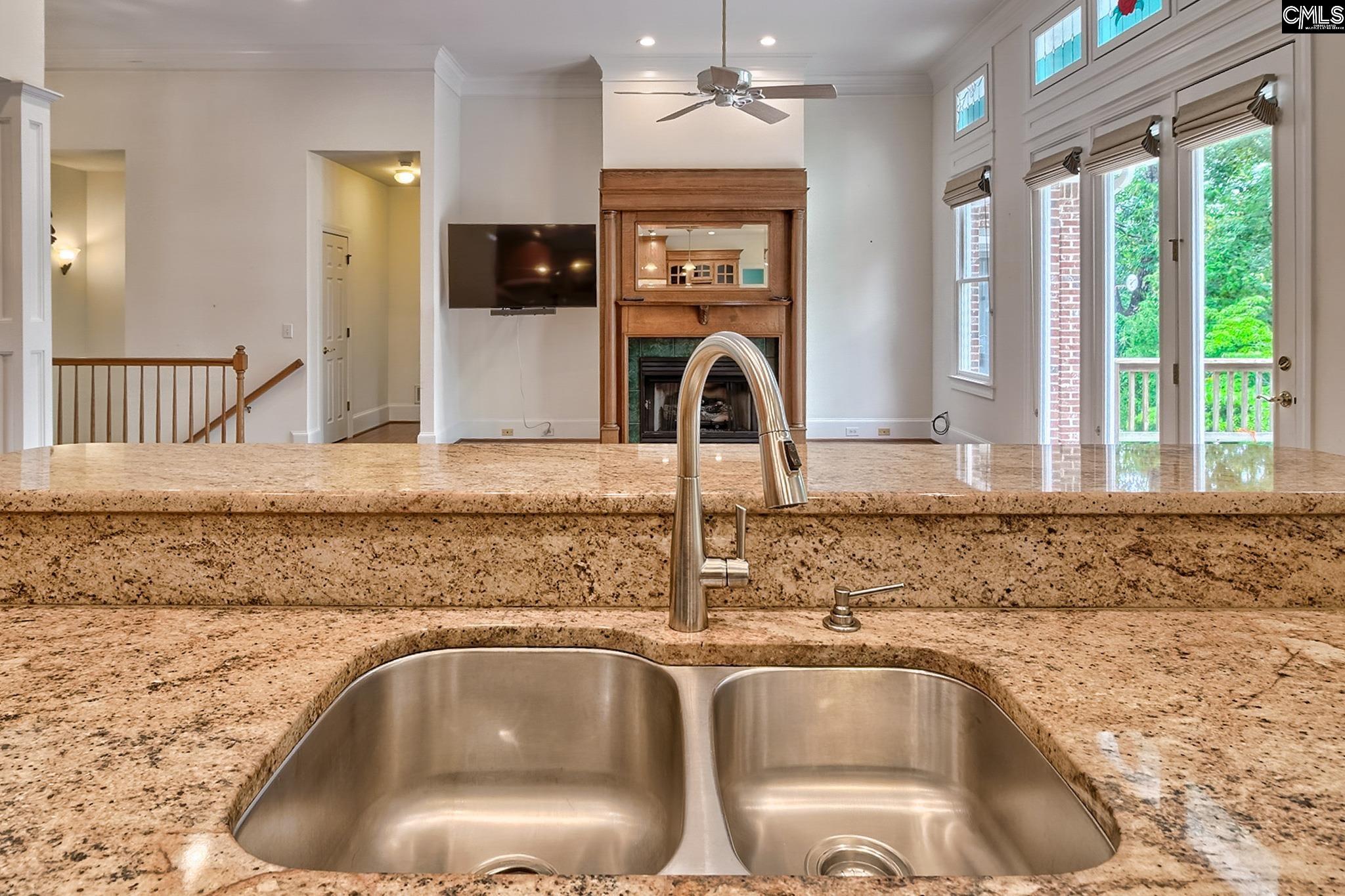 Kitchen with granite counters and a double sink overlooking a living area with a wood fireplace.