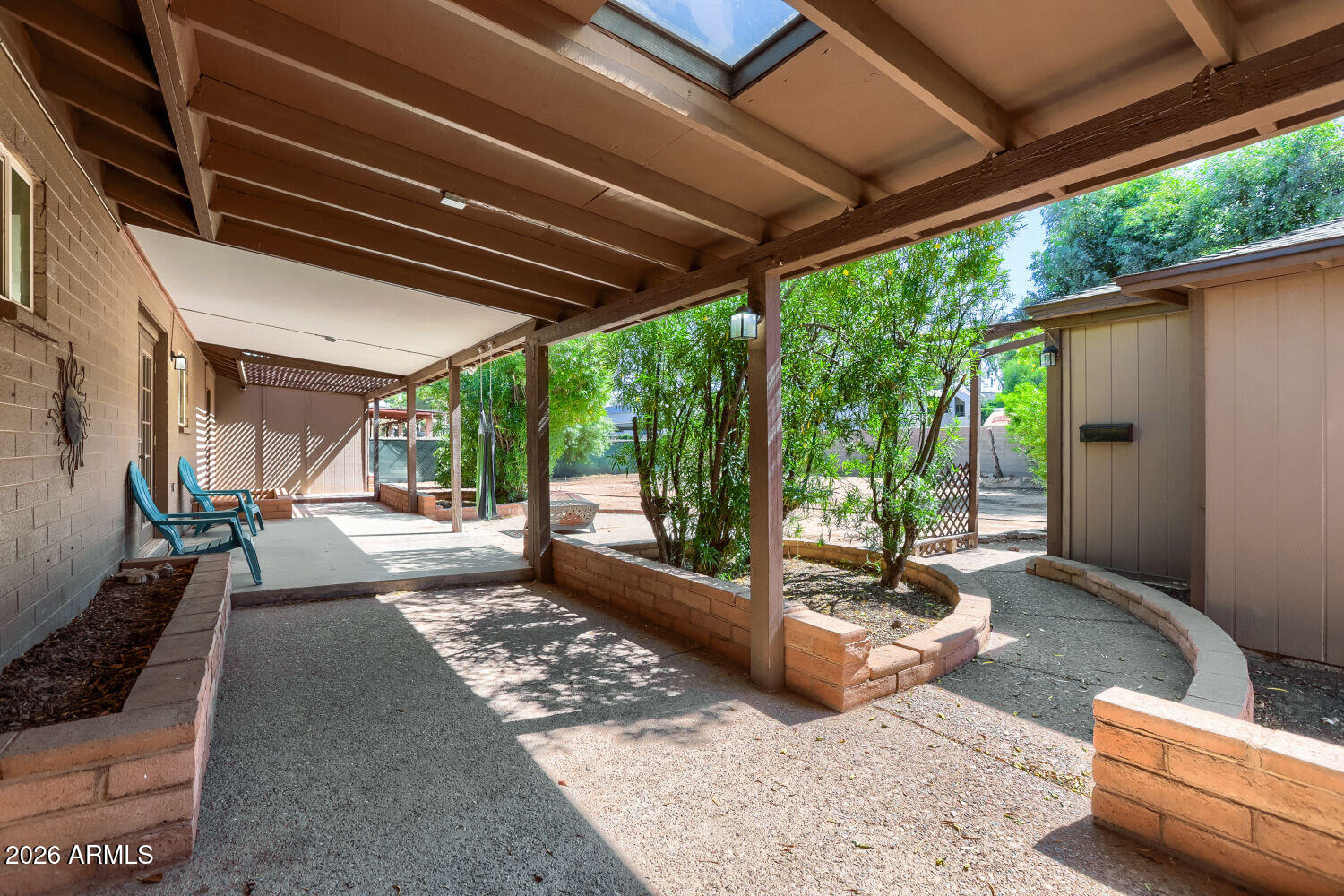 Covered backyard patio with turquoise chairs, raised brick planters, and a skylight.