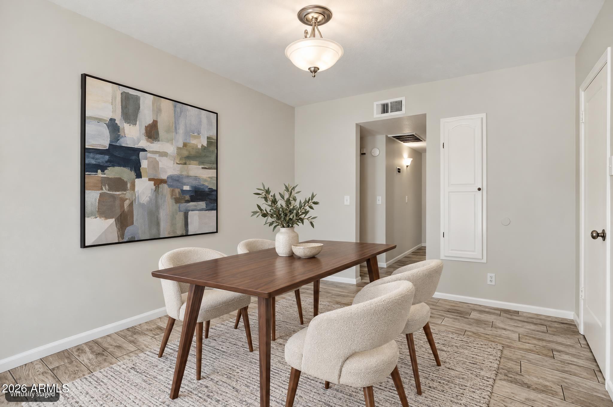 Dining room with a dark wood table, cream chairs, abstract wall art, and wood-look tile flooring.