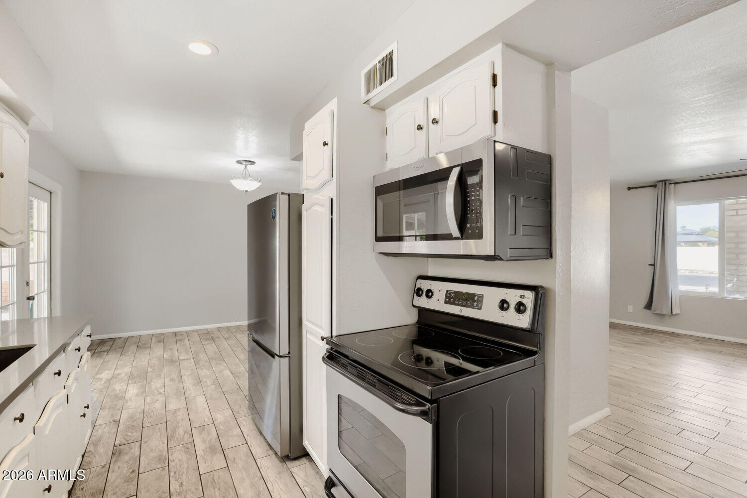 Kitchen with white cabinets, stainless steel appliances, black electric range, and light tile flooring.