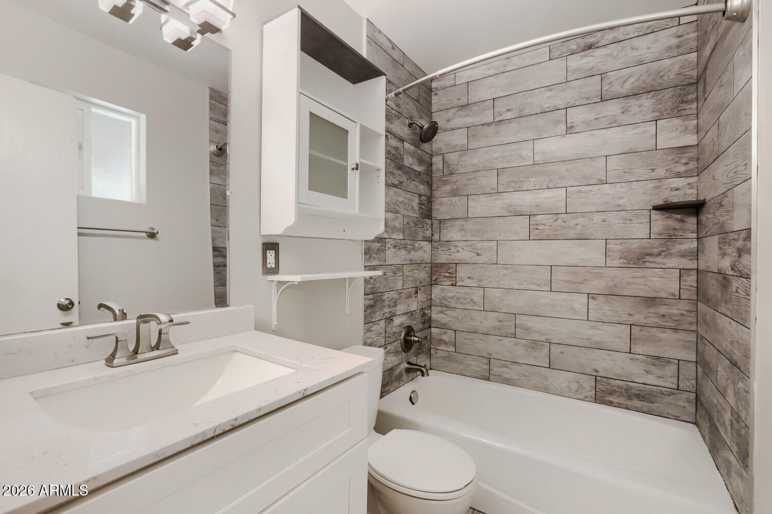 Bathroom with a white vanity and tub surrounded by gray wood-look tile.