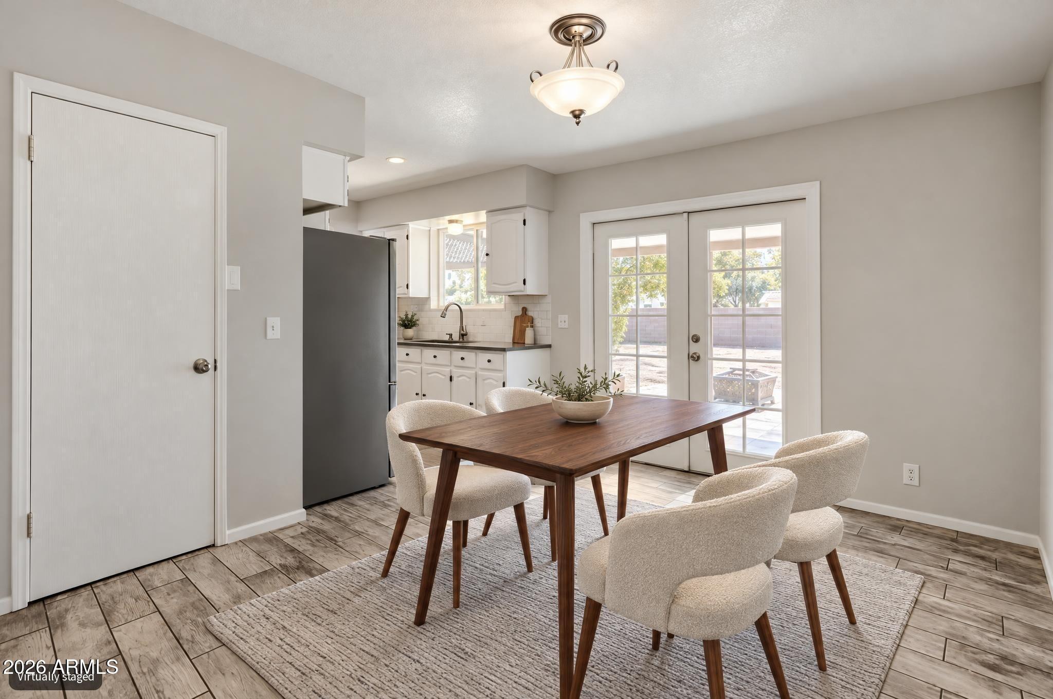 Dining area with a wood table and cream chairs beside an open kitchen and French doors.