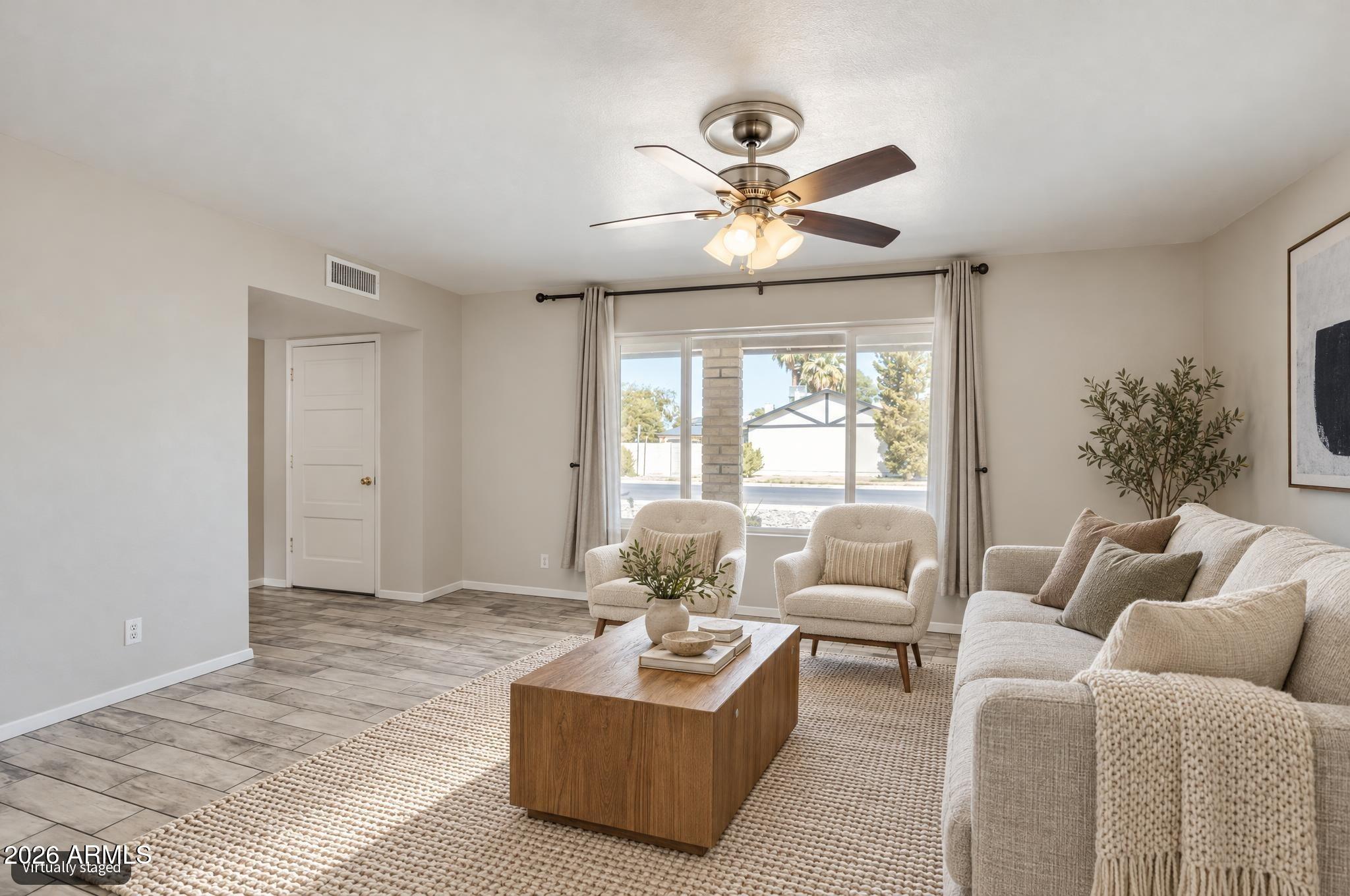 Living room with a light sofa, two armchairs, wooden coffee table, and large curtained window.