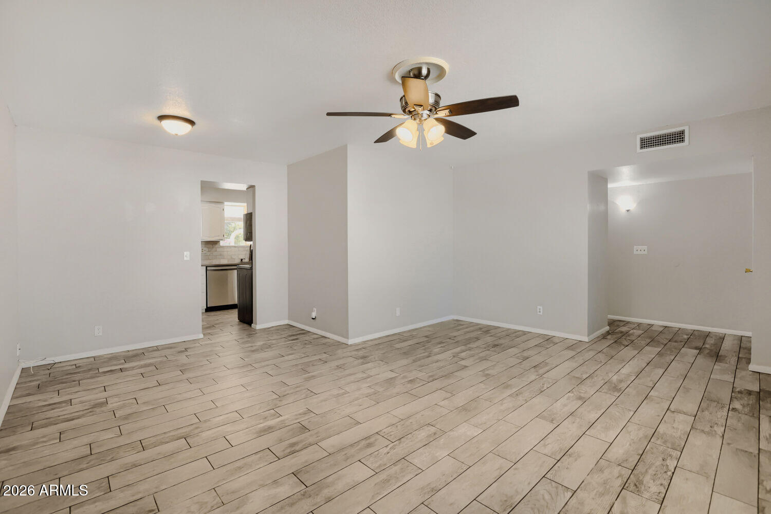 Vacant living room with wood-look tile flooring and a ceiling fan, opening to the kitchen.