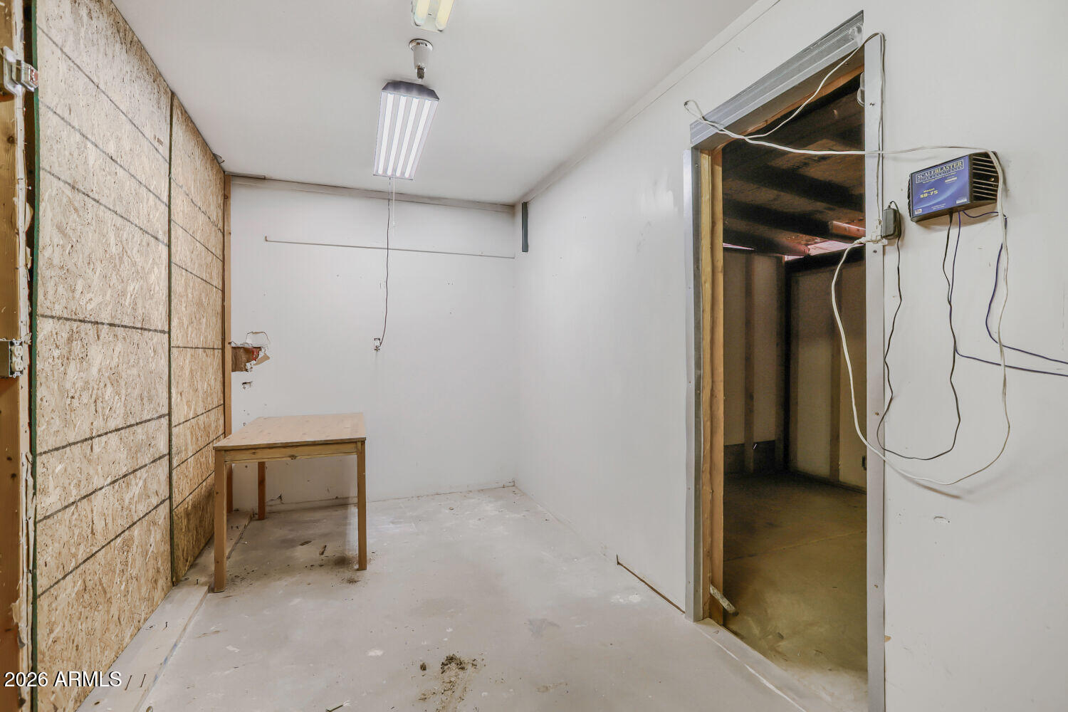 Unfinished garage with plywood wall panels, a small worktable, and an open doorway.