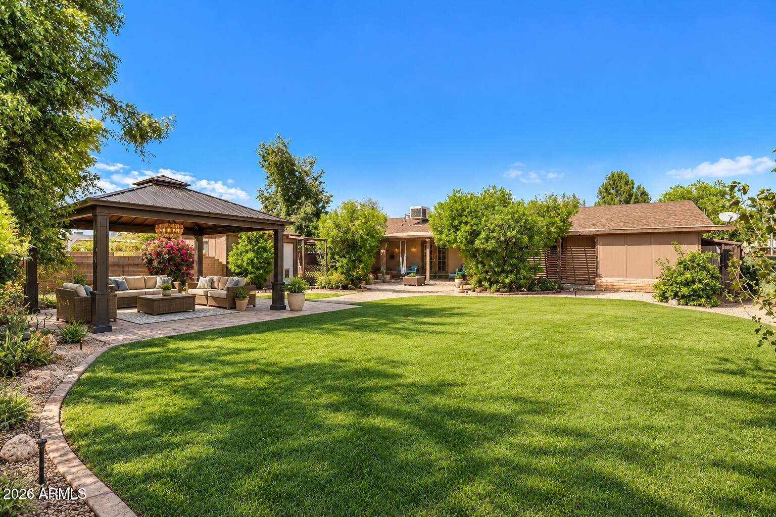 Backyard with a broad lawn, covered gazebo seating area, landscaped beds, and a single-story home.