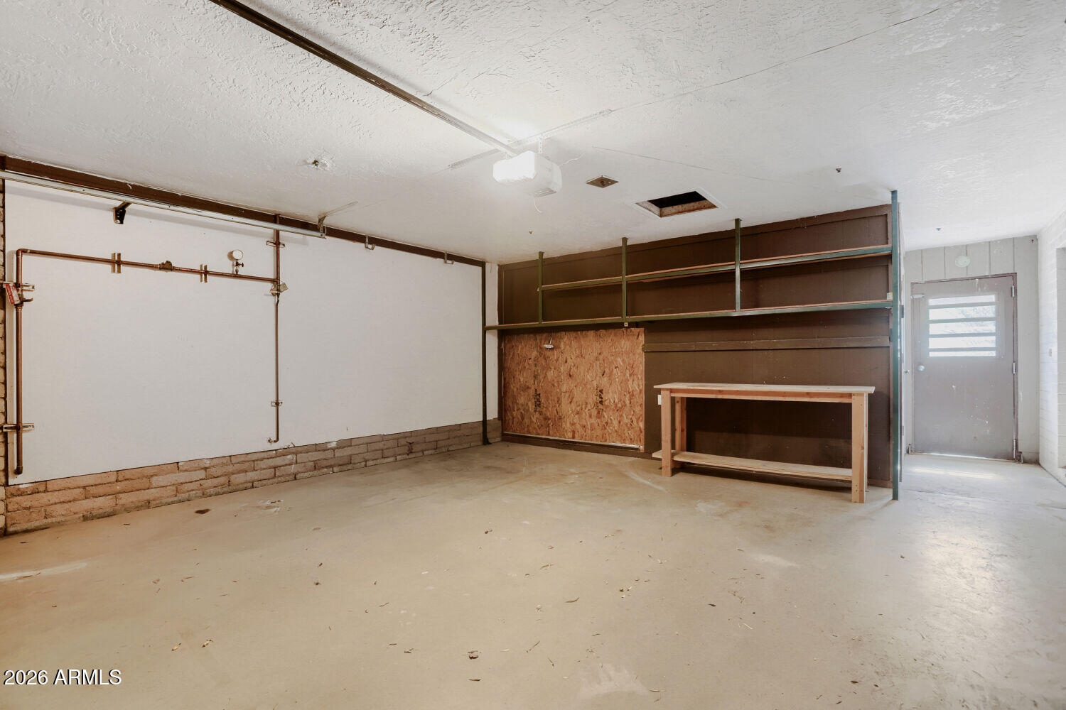 Empty garage with exposed pipes, metal shelving, and a workbench.