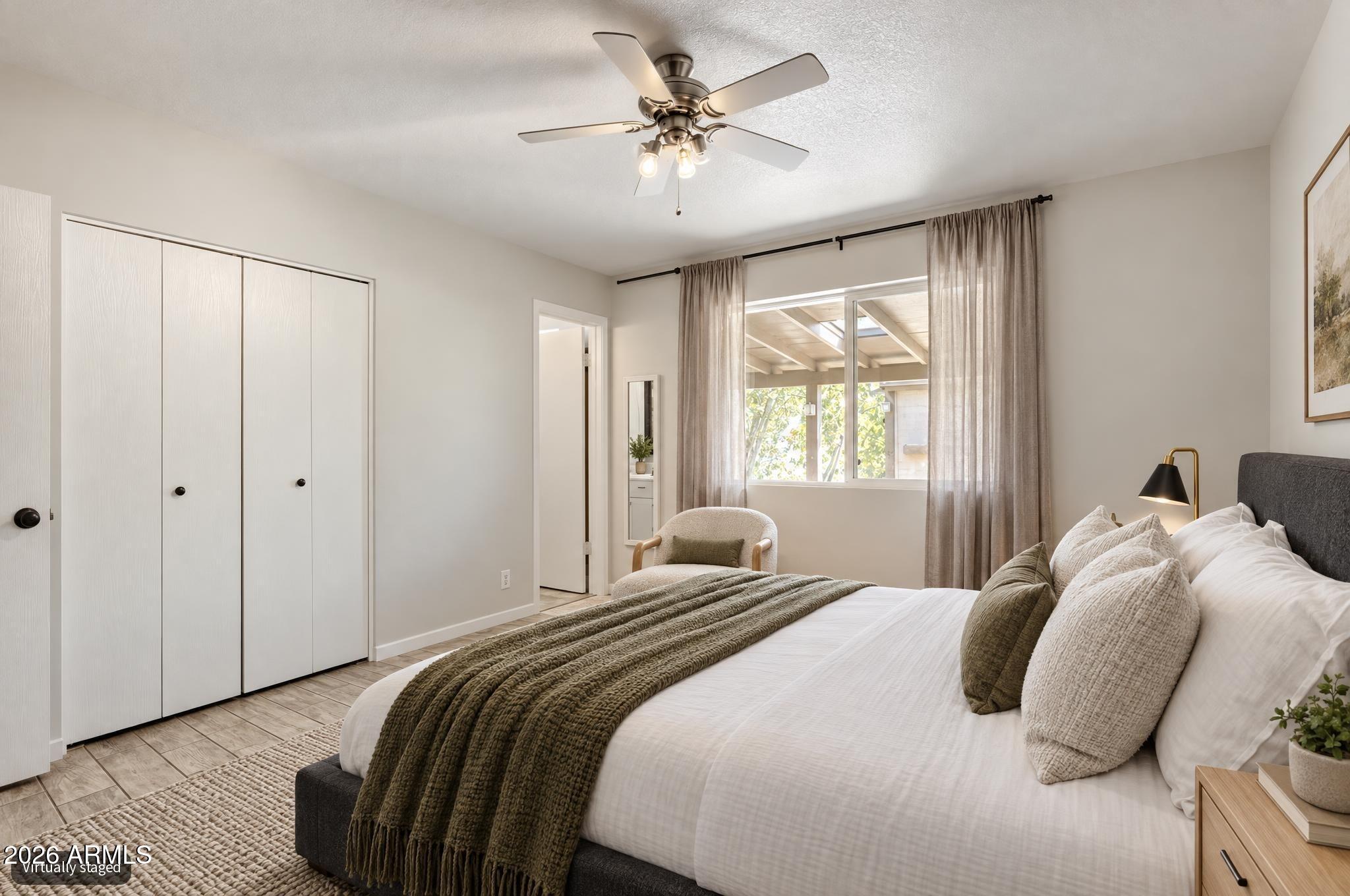 Bedroom with a white bed, dark green throw, ceiling fan, and window overlooking a covered patio.