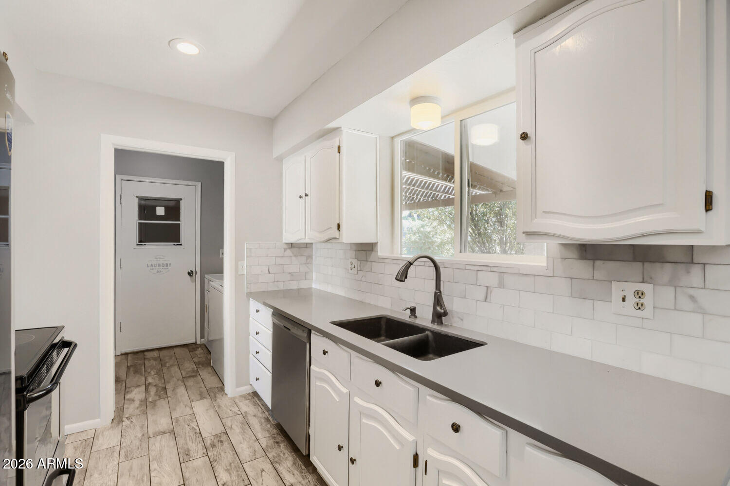 Kitchen with white cabinets, gray counters, a double sink, and a doorway to the laundry area.