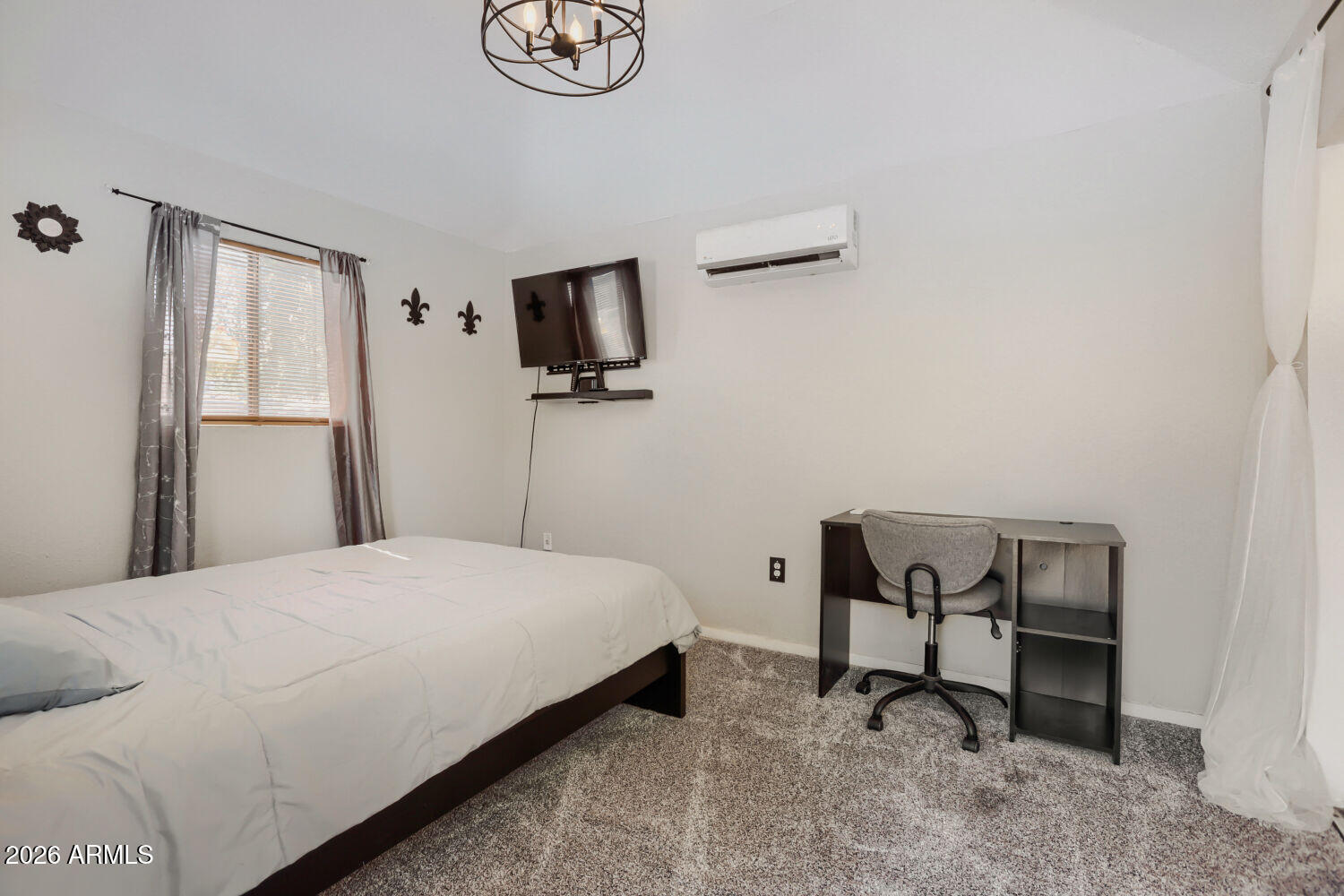 Bedroom with a wall-mounted television, mini-split air conditioner, and desk beside the bed.
