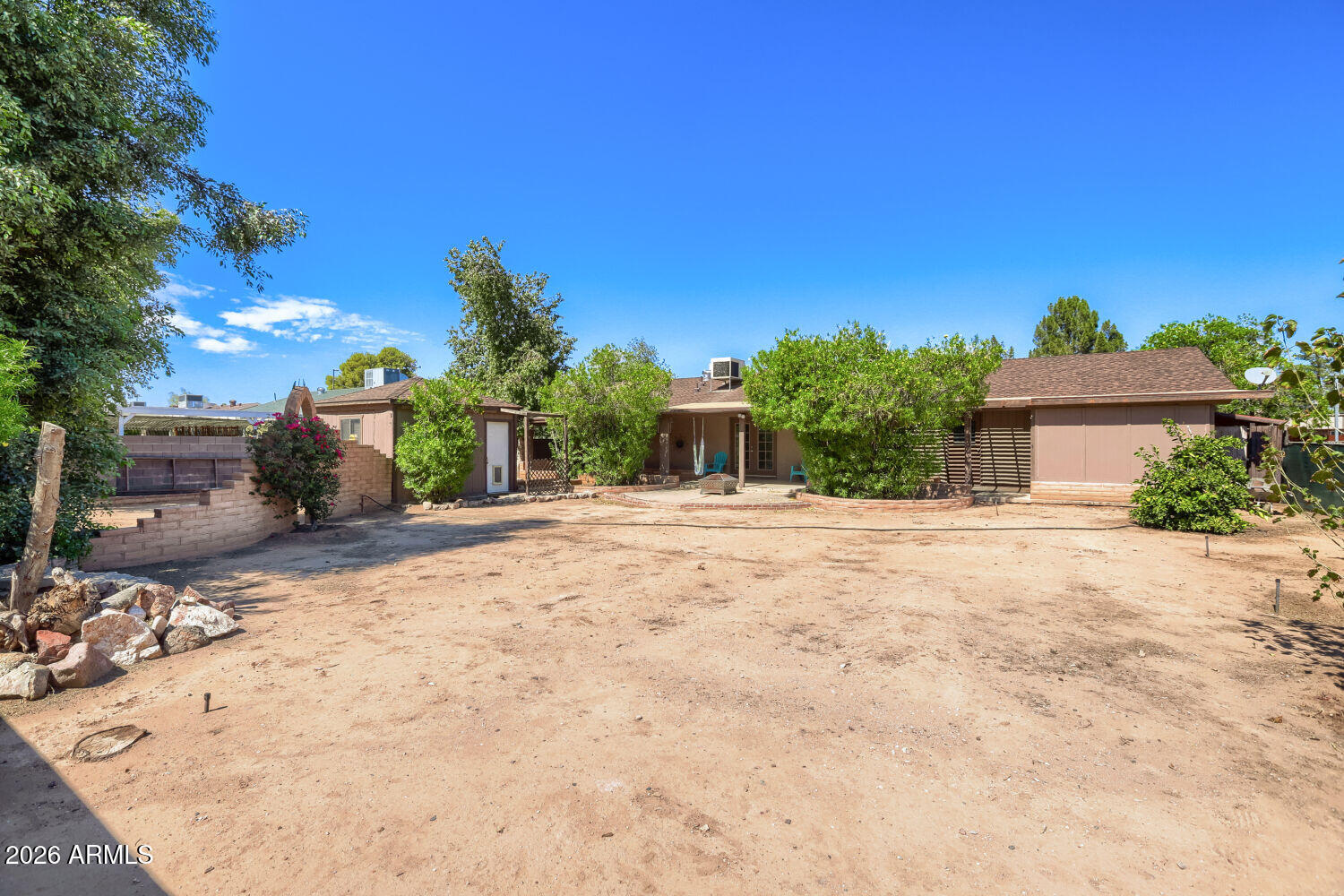 Backyard with a covered patio, outdoor seating, mature trees, and a broad dirt yard.