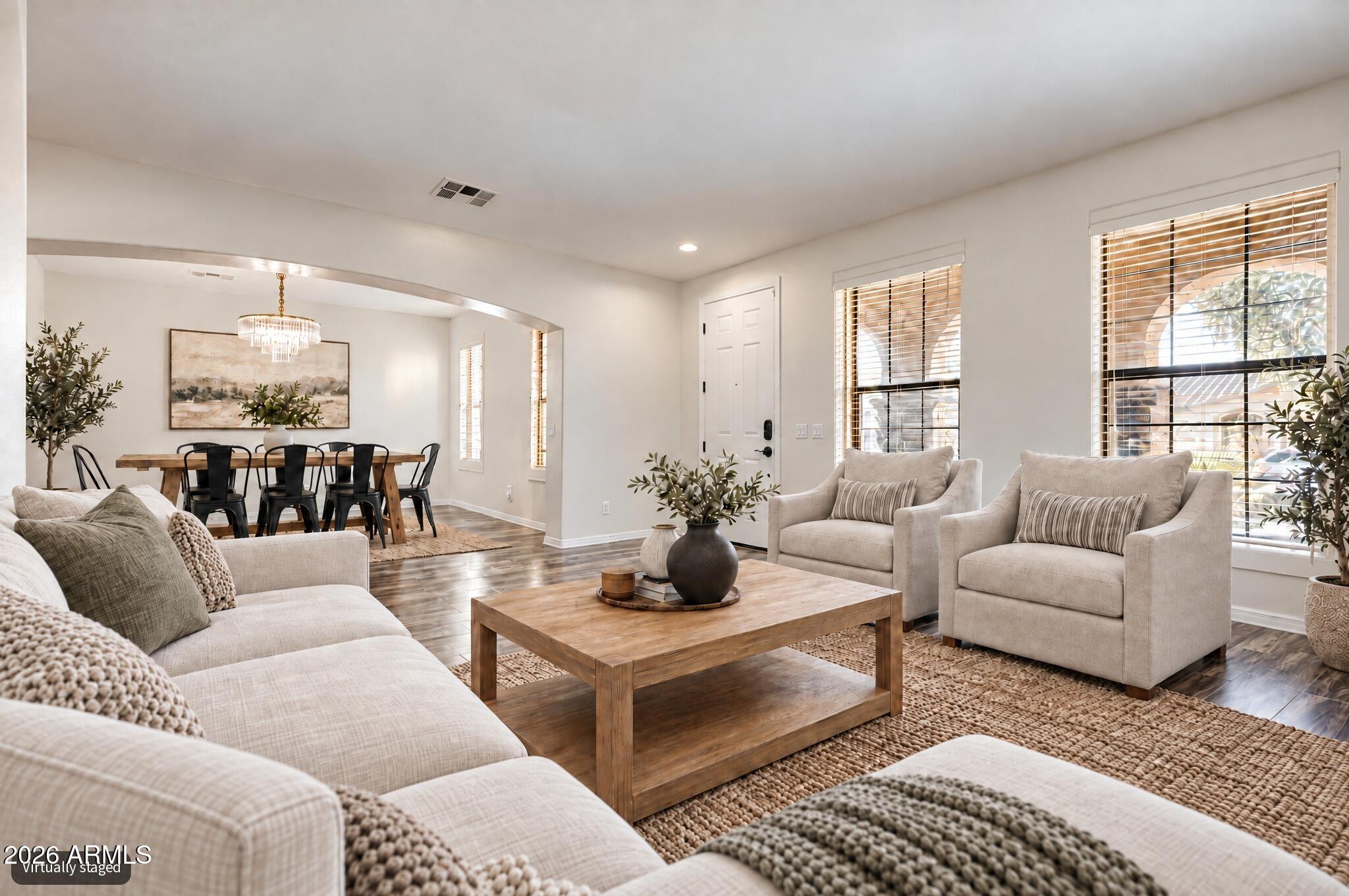 Staged living room with light seating, a wood coffee table, and an adjoining dining area.