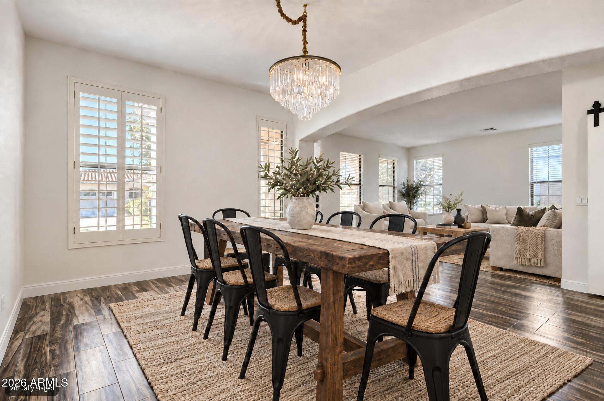 Dining room with a rustic wood table and crystal chandelier opening onto a bright living room.
